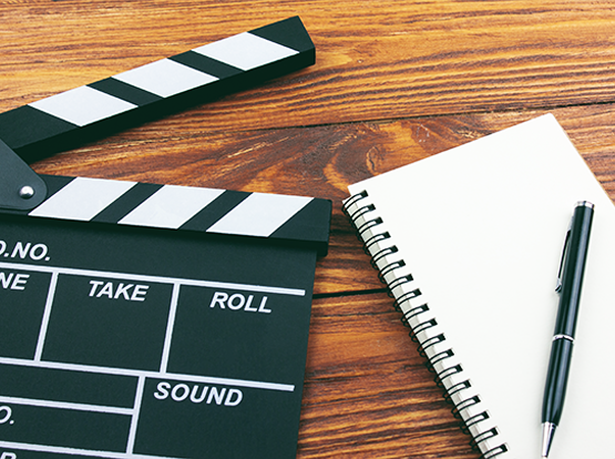 Clapperboard, spiral notebook, and pen on a wooden desk representing OC Videography’s film production planning, shot lists, and creative pre-production process.