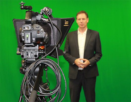 Professional videographer filming a man in a suit against a green screen backdrop representing OC Videography green screen production and corporate video editing services.
