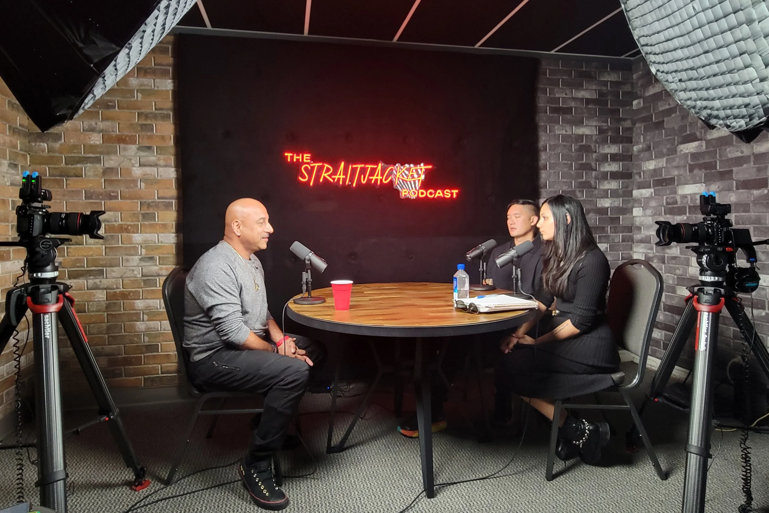Professional podcast production setup with multiple cameras and microphones recording a conversation at a studio table. High-quality audio and multi-camera filming by OC Videography.