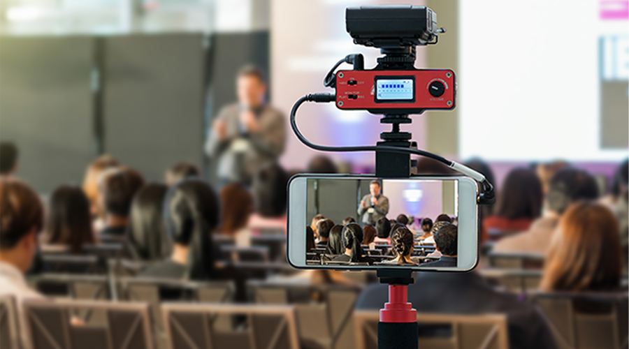 Camera on tripod recording a speaker during a conference presentation representing OC Videography corporate event coverage and live filming services in Orange County and Los Angeles.