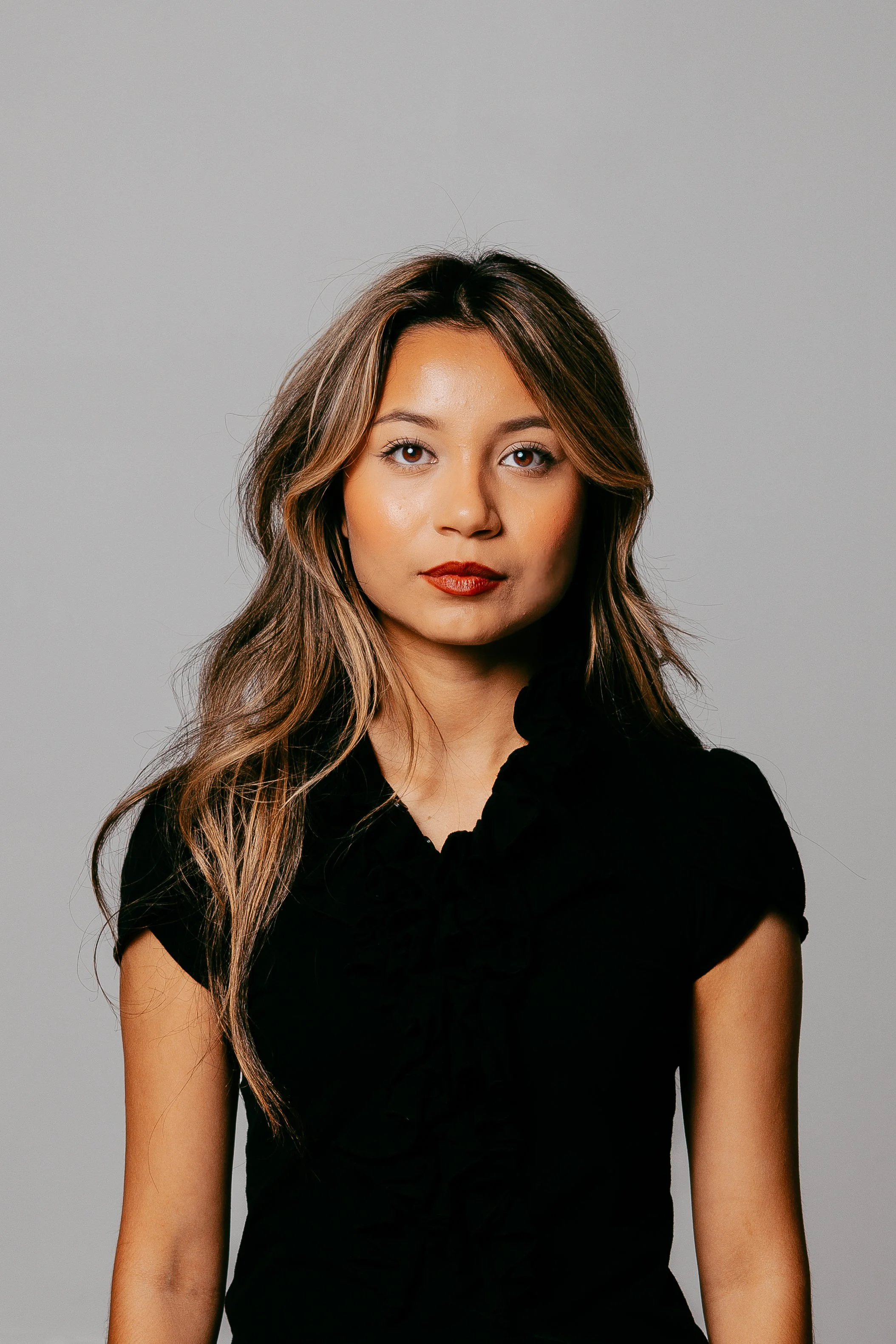 A smiling man with glasses, a beard, and a yellow and black cap holding a camera on his shoulder, standing against a plain white background.