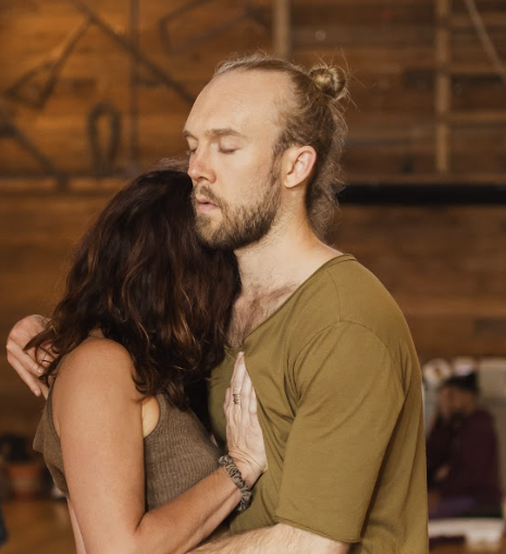 A couple participant of Facilitator Certification  dancing closely in a dimly lit room with wooden walls, eyes closed and embracing each other.