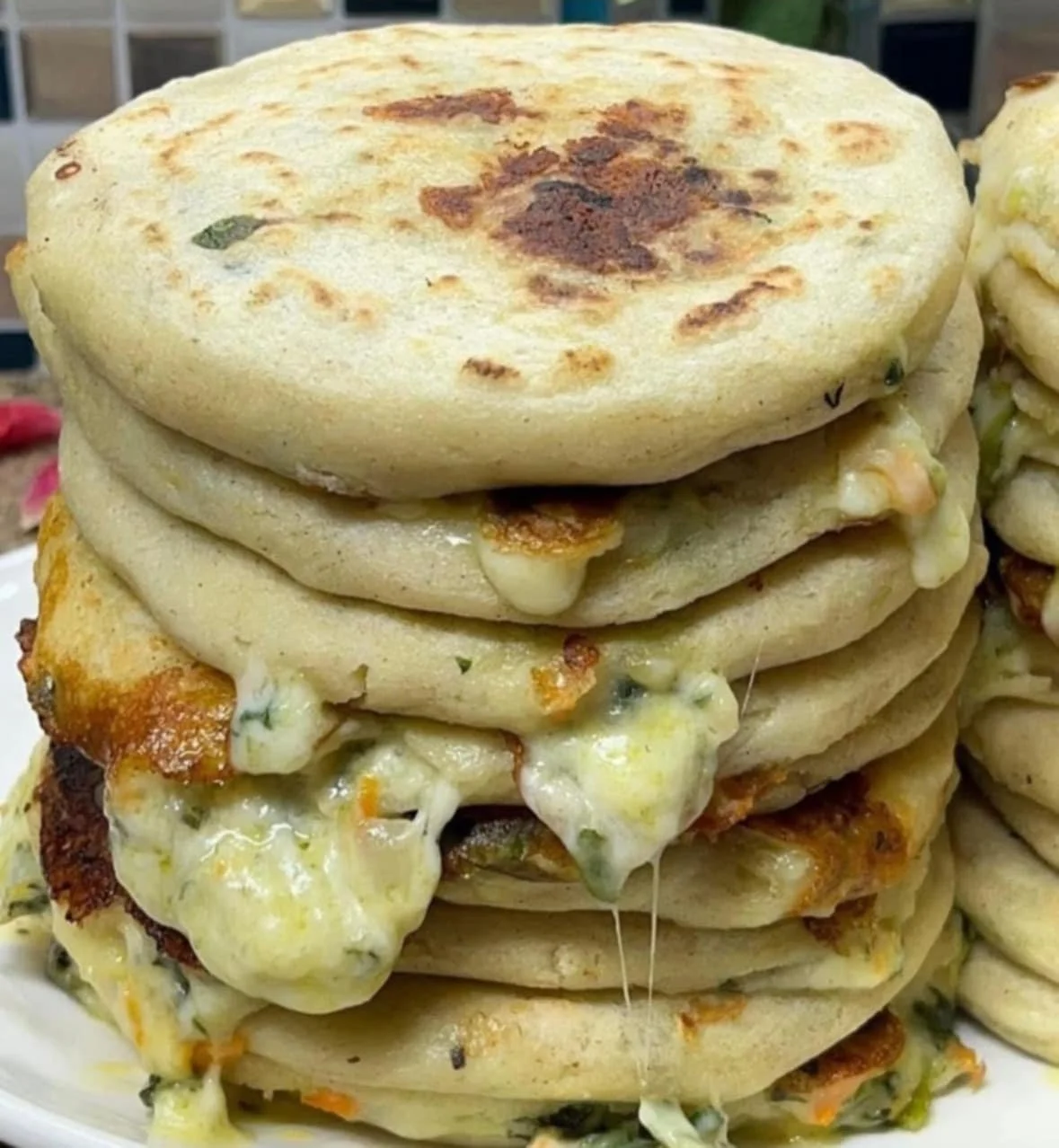 Stack of stuffed bread or flatbreads with melted cheese and fillings, possibly vegetables and meat.