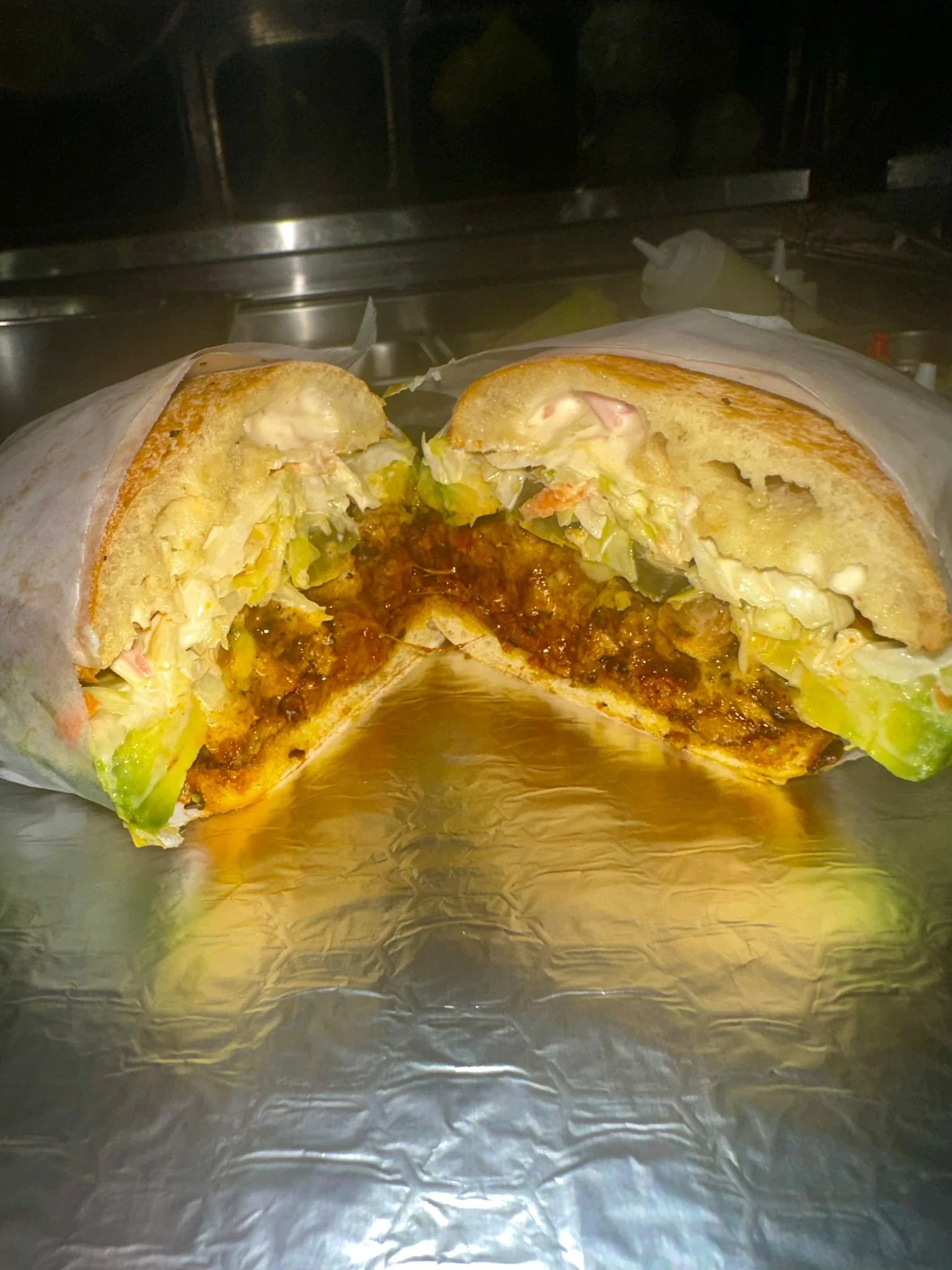 Half eaten burger with lettuce, tomato, cheese, and beef patty wrapped in paper, on a metallic surface.