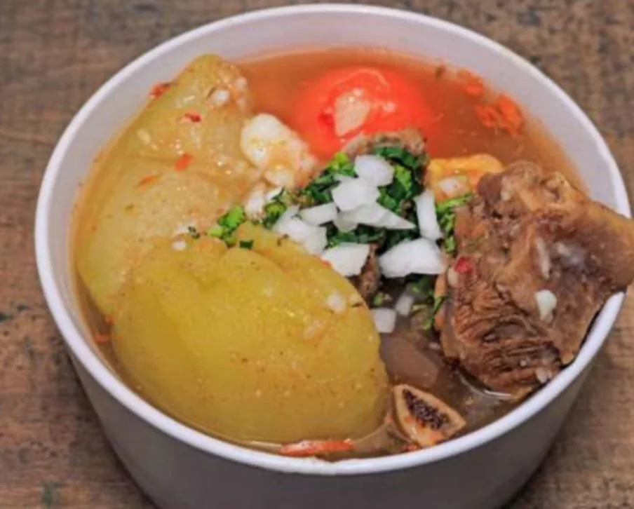 Bowl of Mexican menudo soup with tripe, potatoes, spices, chopped onions, and cilantro.