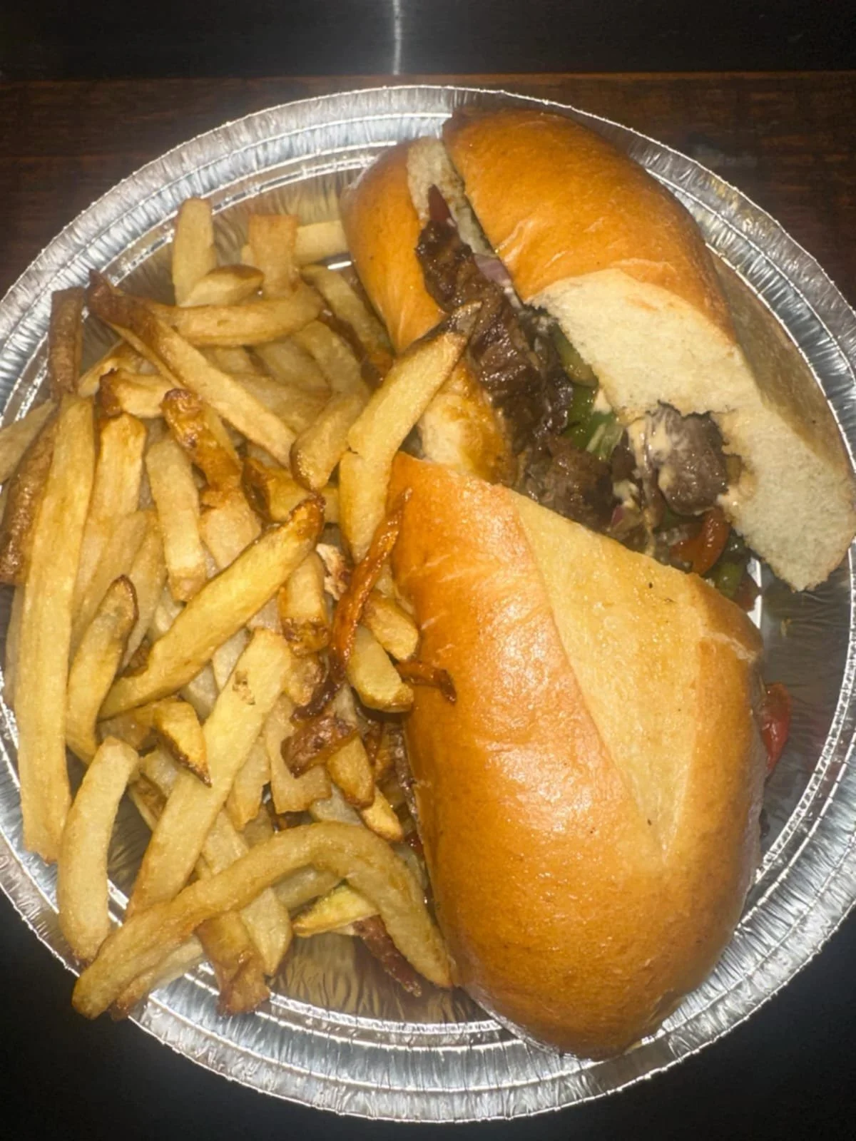 A foil container holding two beef sandwiches and a serving of French fries.