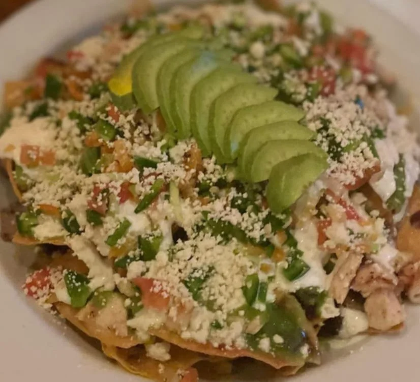 Plate of Mexican nachos topped with sliced avocado, crumbled cheese, diced tomatoes, and chopped green onions.