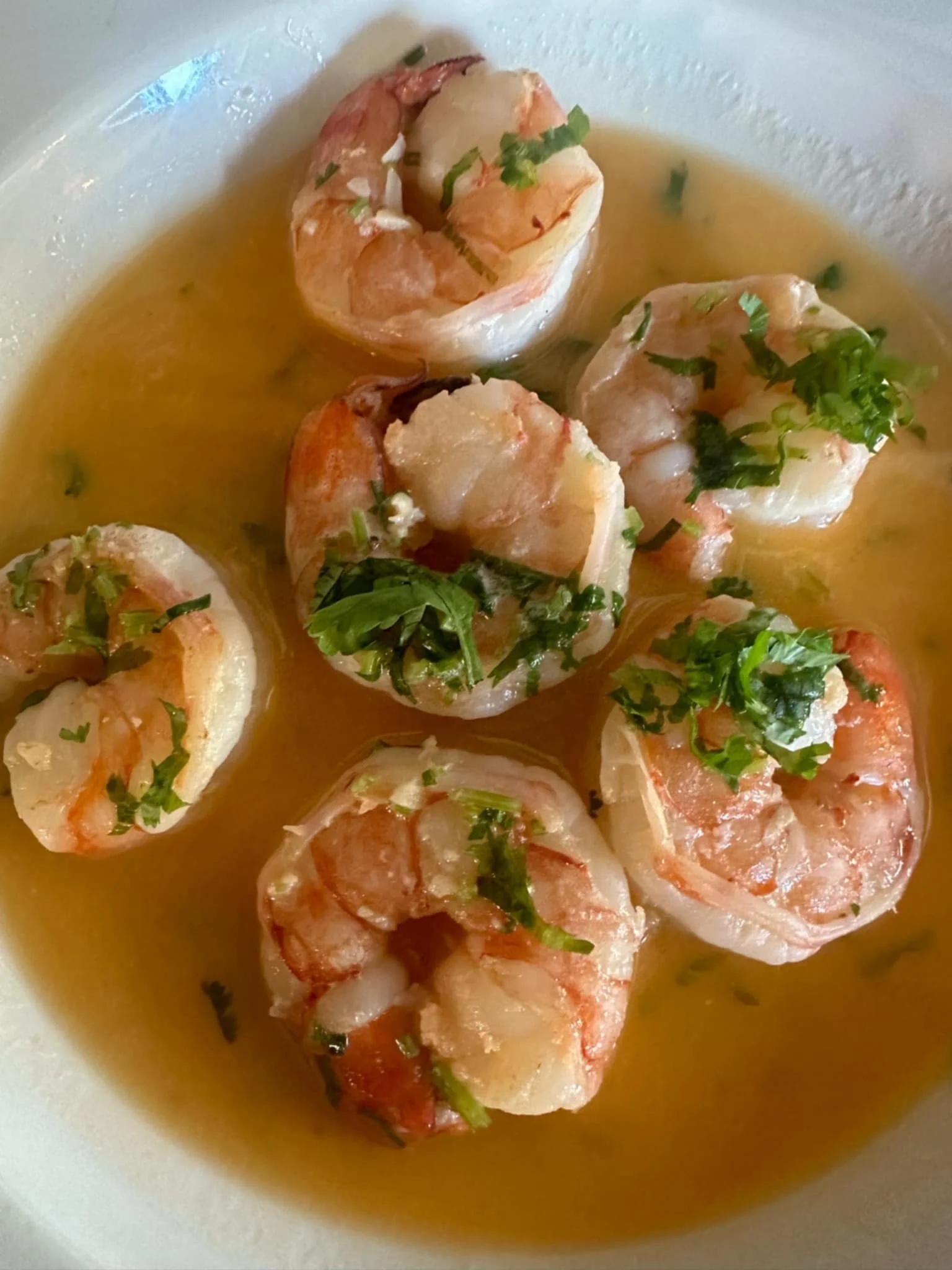 Cooked shrimp garnished with chopped parsley in a light broth