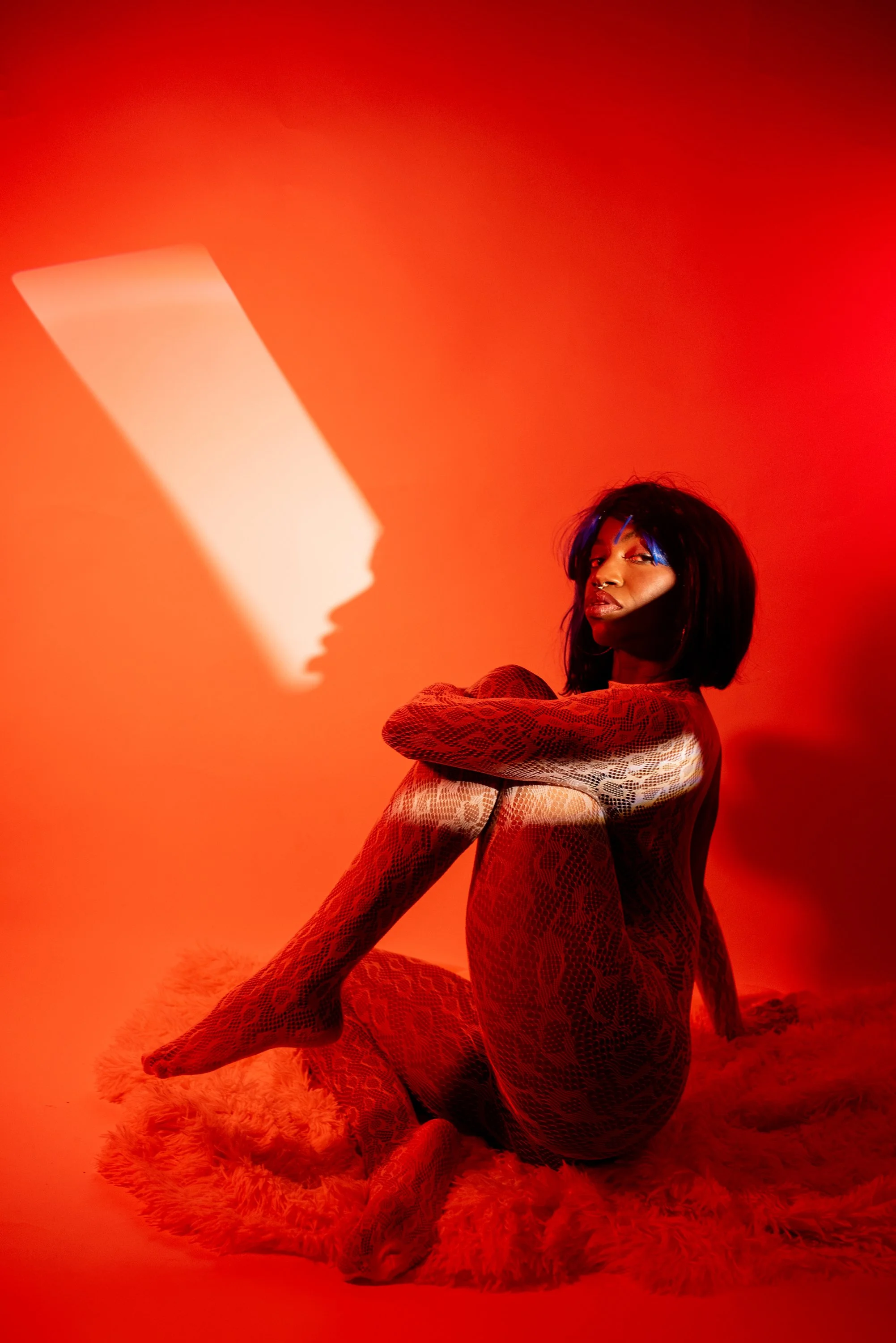 Red light boudoir  session with Djau, showcasing bold lighting and elegant pose.