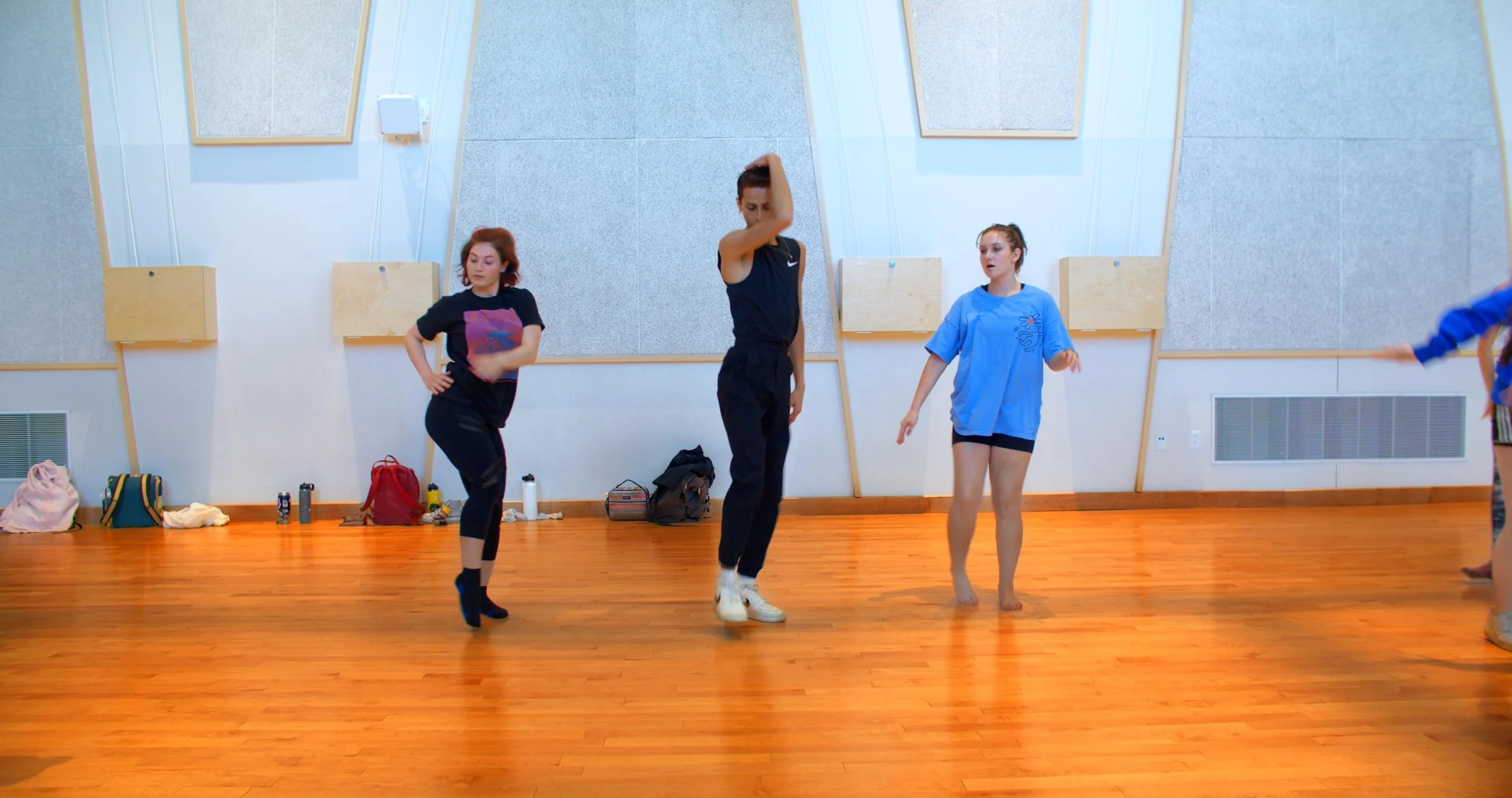 Group of young women practicing dance in a studio with wood floors and soundproof walls.