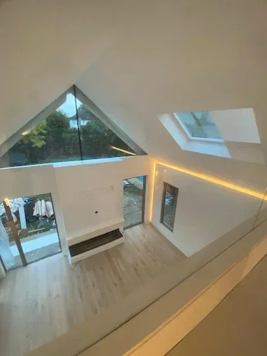 Interior view of a modern, minimalistic room with large triangular window, wooden flooring, and skylight, viewed from above.