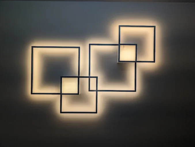 Modern wall art featuring interconnected black square frames with illuminated backgrounds creating geometric shadow patterns.