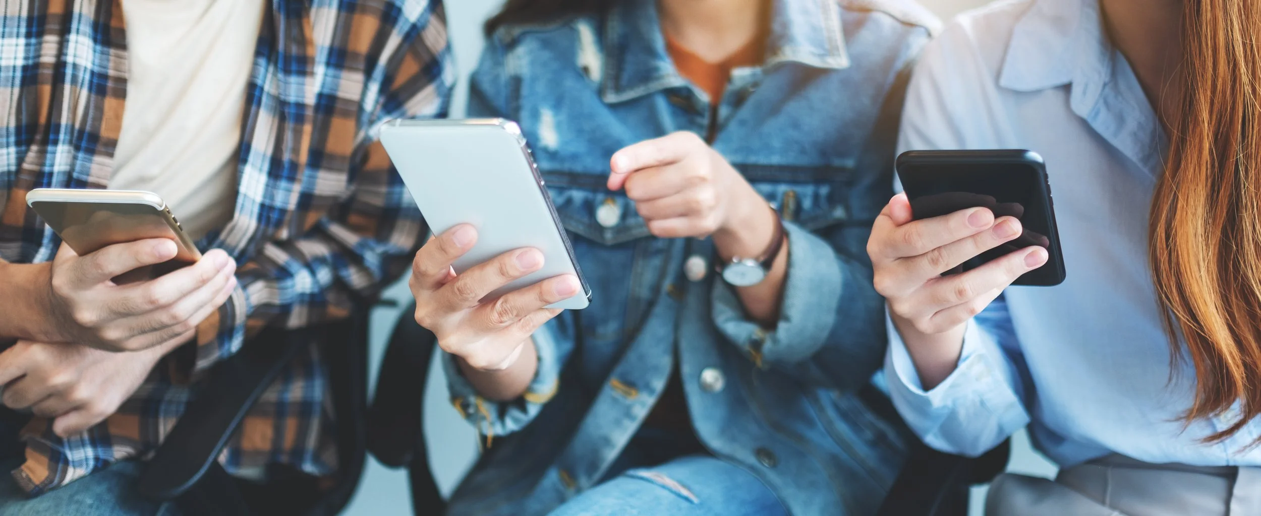 Three people sitting close together, each holding a smartphone and looking at their screens.