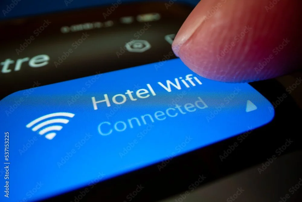 Close-up of a finger tapping a smartphone screen showing Wi-Fi connection options, with the 'Hotel Wifi' network selected as connected.