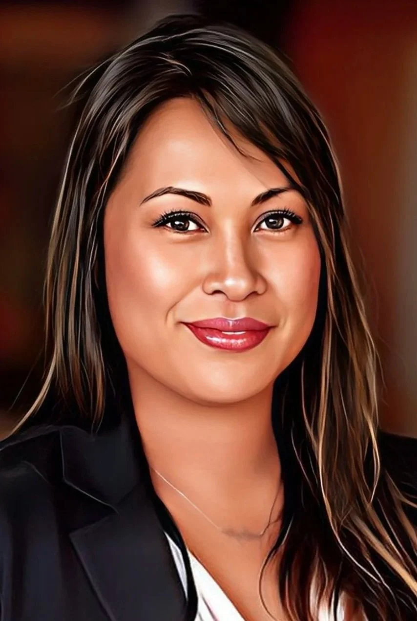 Close-up portrait of a woman with long, wavy, dark hair with lighter highlights, smiling softly, wearing makeup, a black blazer, and a white top, with a blurred warm-toned background.