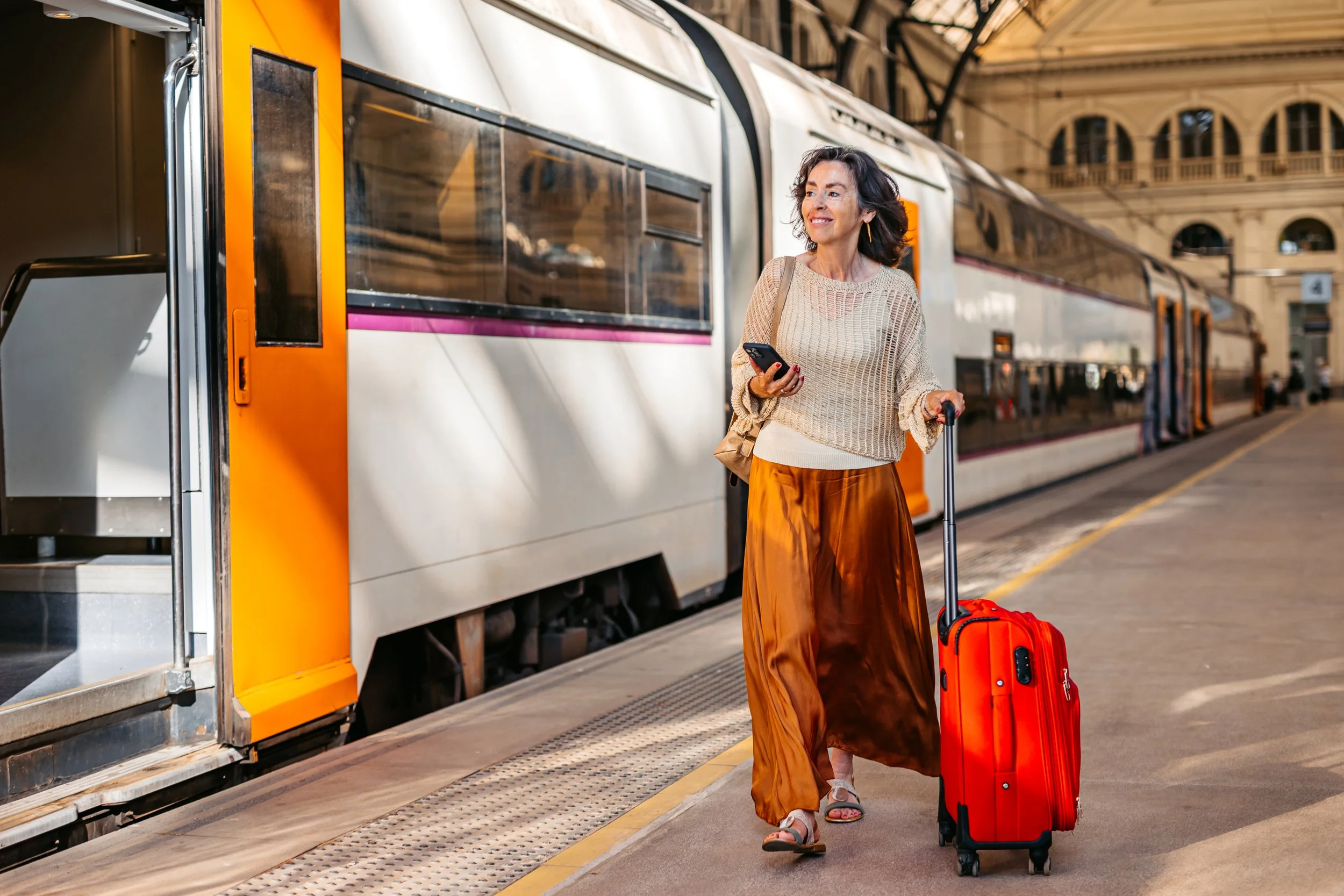 A woman with a suitcase and a phone at a train station.