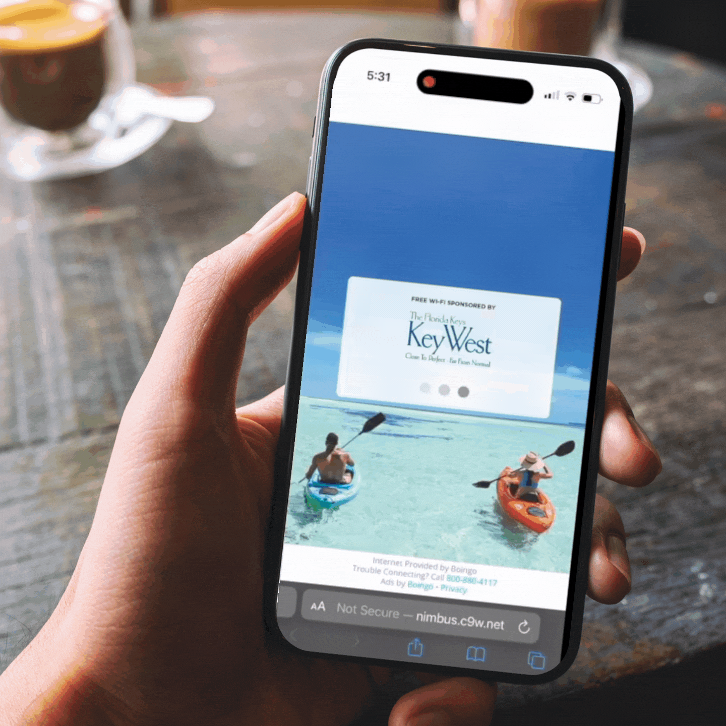 Person holding a smartphone displaying an advertisement for Key West, featuring two people kayaking in clear water.