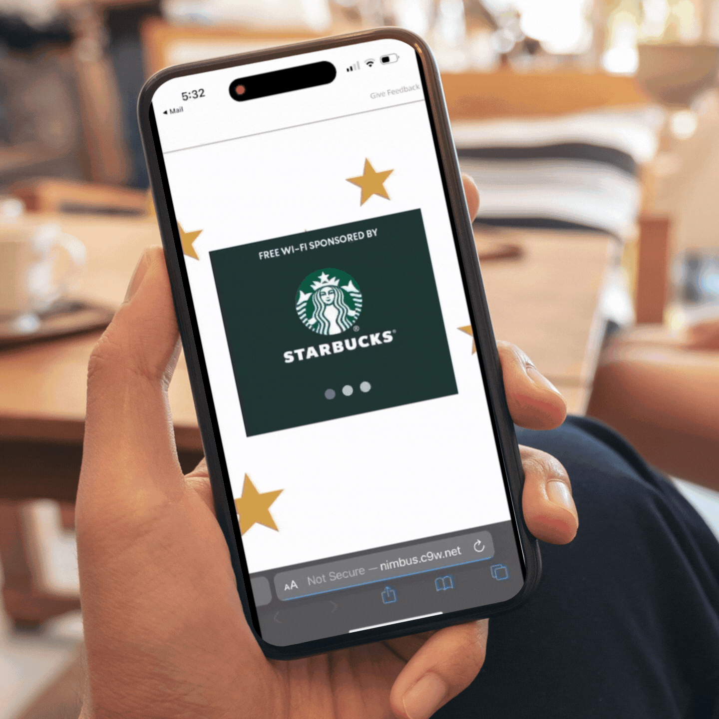 A person is holding a smartphone displaying a webpage with the Starbucks logo and advertising free Wi-Fi sponsored by Starbucks, decorated with gold star illustrations, in a cafe setting.