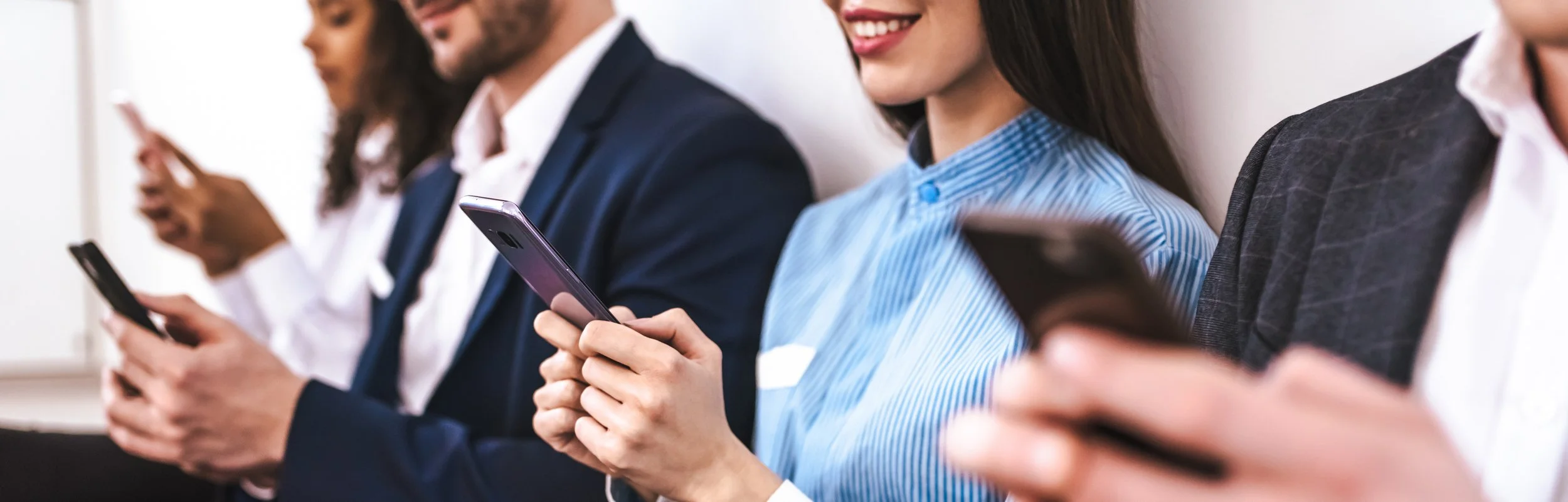 People sitting in a row, looking at their smartphones in a professional setting.
