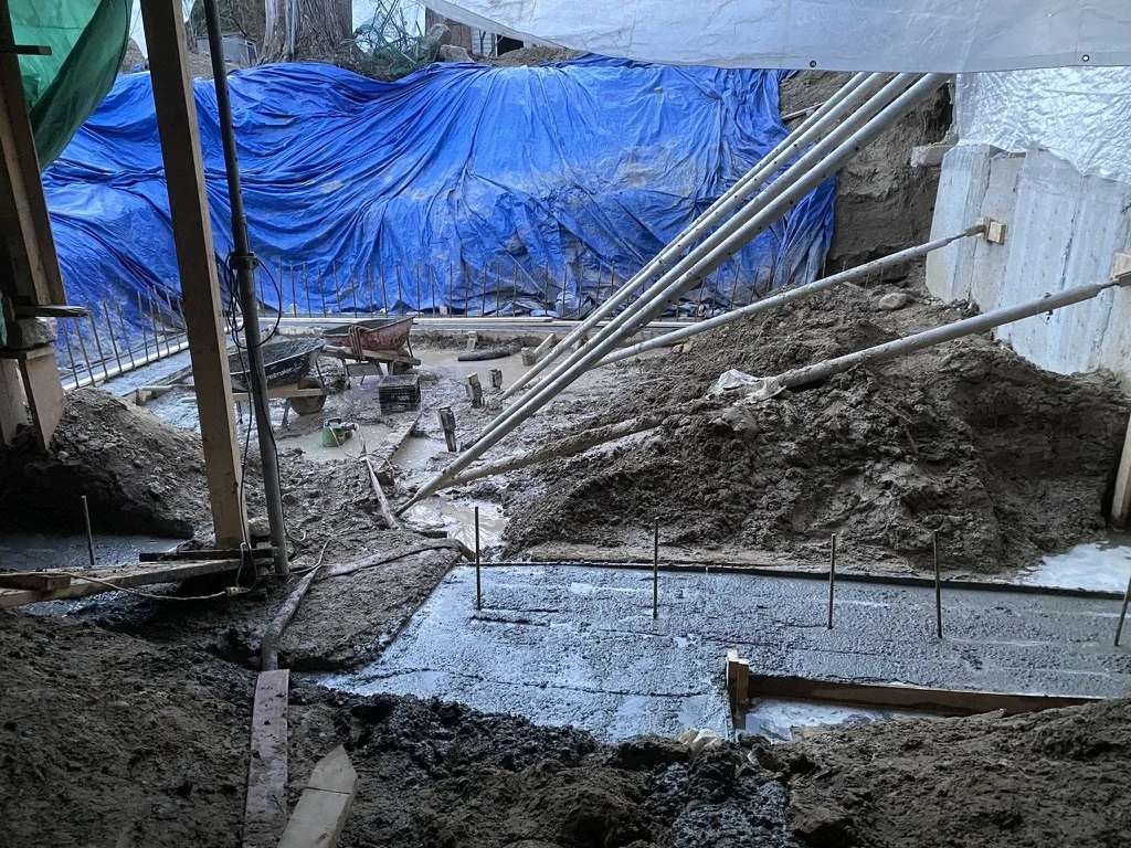 Construction site with exposed dirt, concrete work, and support beams for a building foundation.