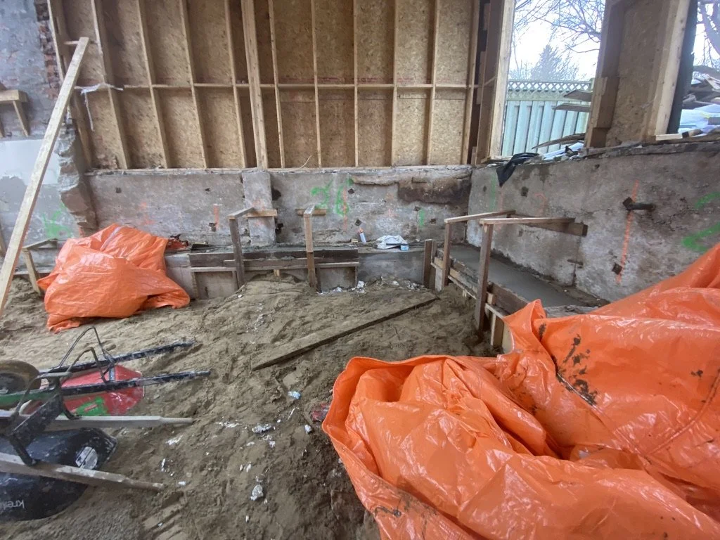 Construction site with exposed wall studs, dirt floor, and orange construction tarps.