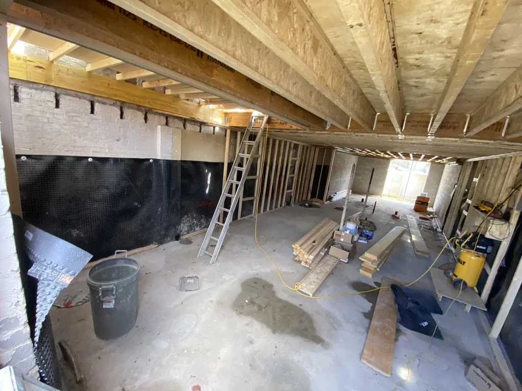 Interior of a building under construction with wooden framing, construction tools, and materials scattered on the concrete floor.