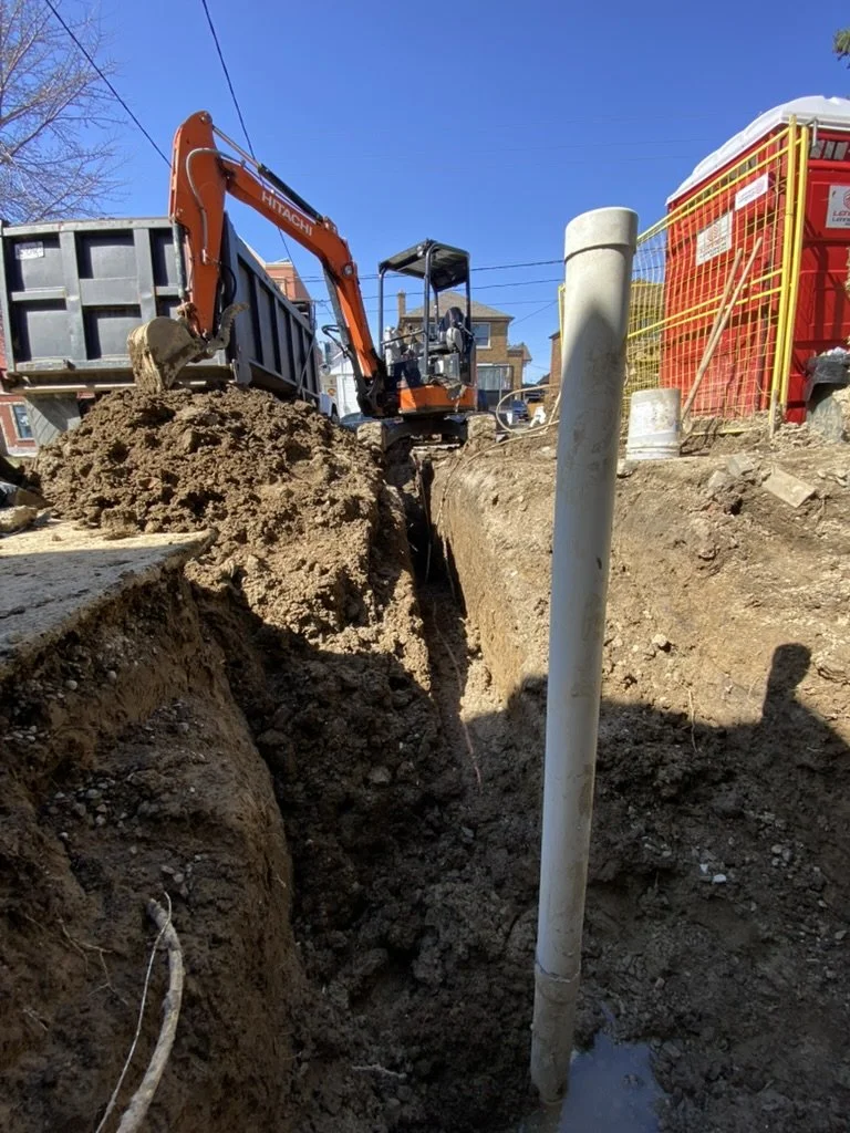 Construction site with an excavator digging a trench for utility poles and pipes.