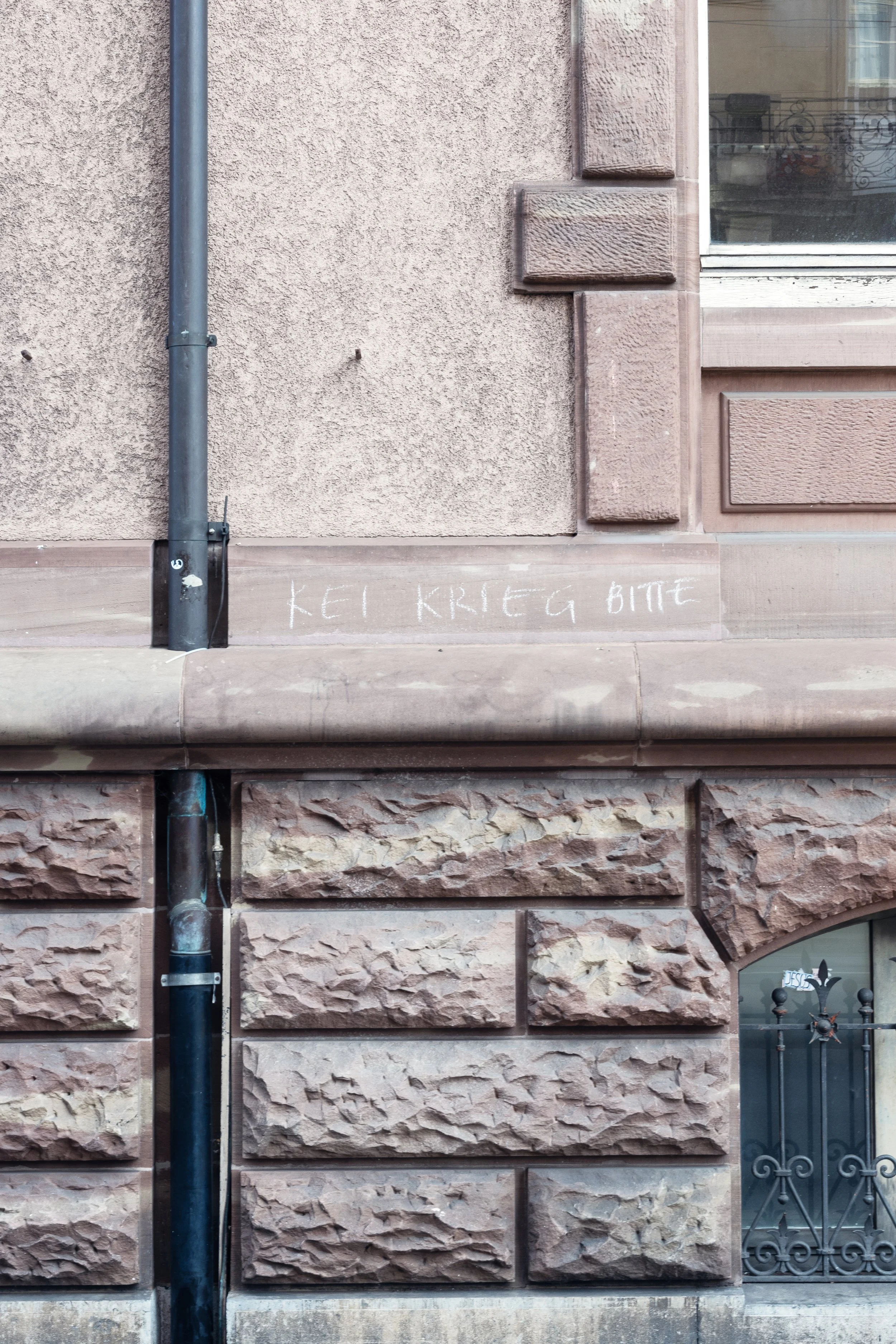 A mauve wall in Basel that says "no more war please" in Swiss german