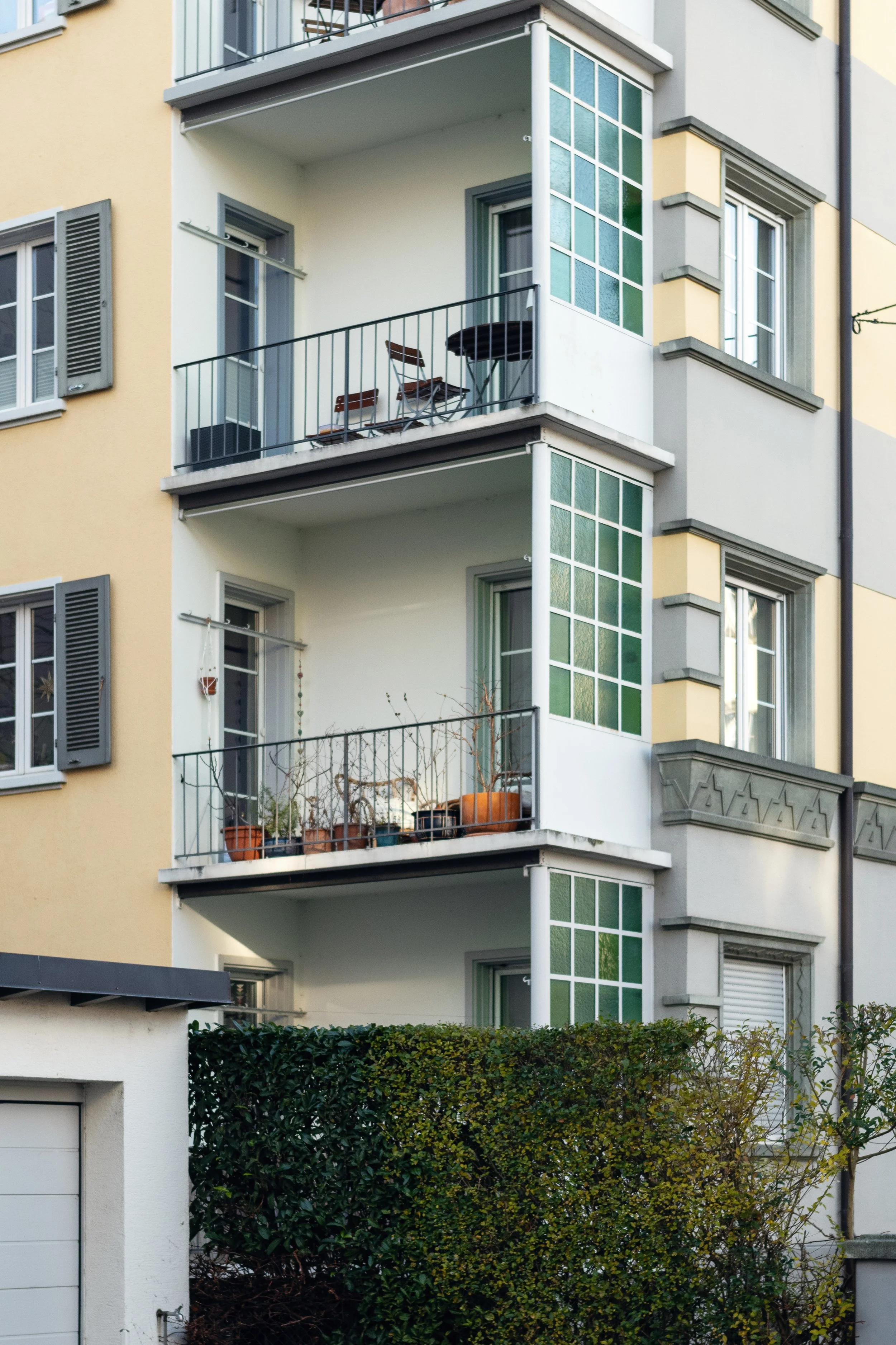 Close-up of a yellow and green multi-story residential building with balconies, potted plants, and outdoor furniture in Basel, Switzerland.