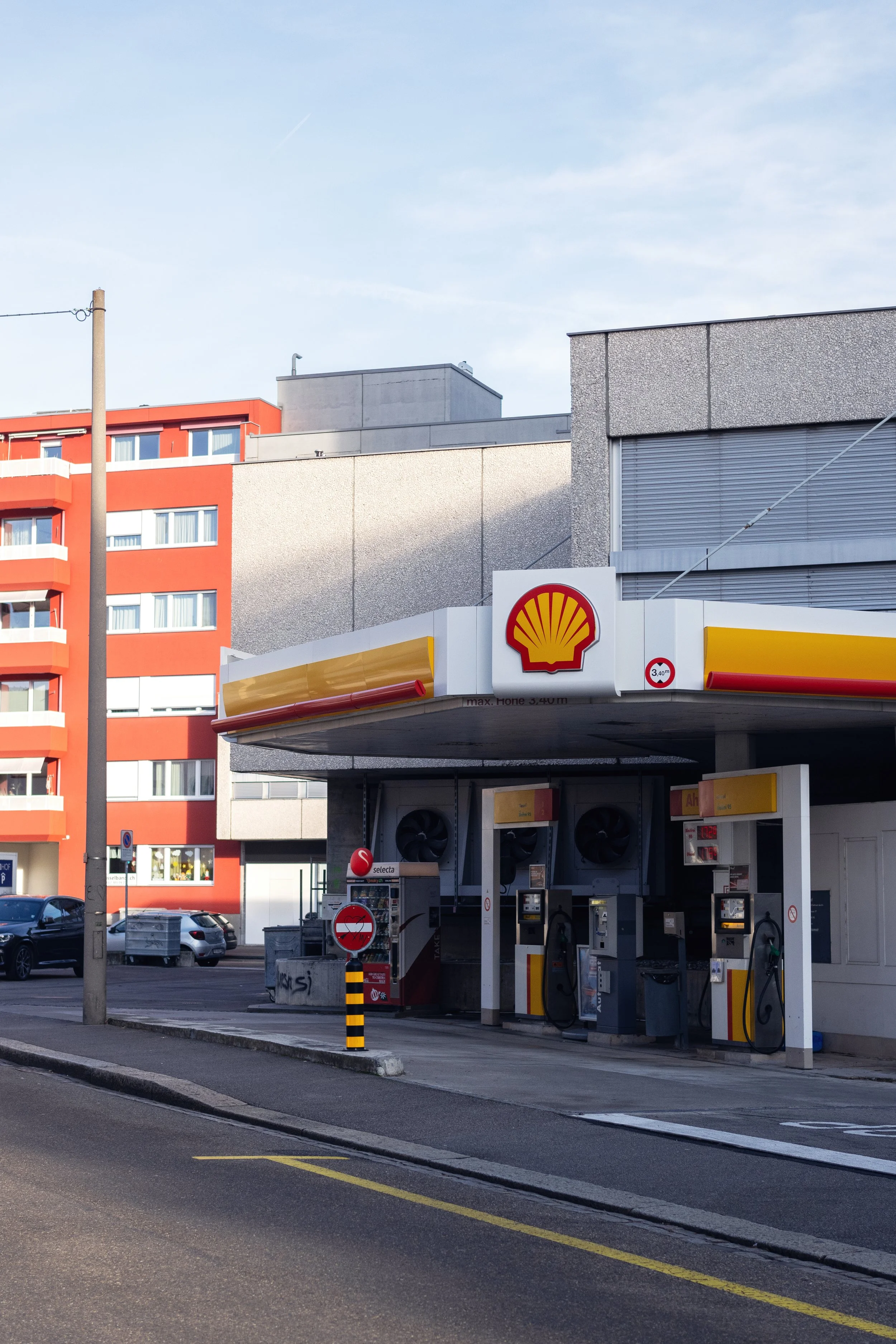 Shell gas station with fuel pumps in the city-centre of Basel, Switzerland, multi-story red, gray, and concrete buildings in the background, clear sky.