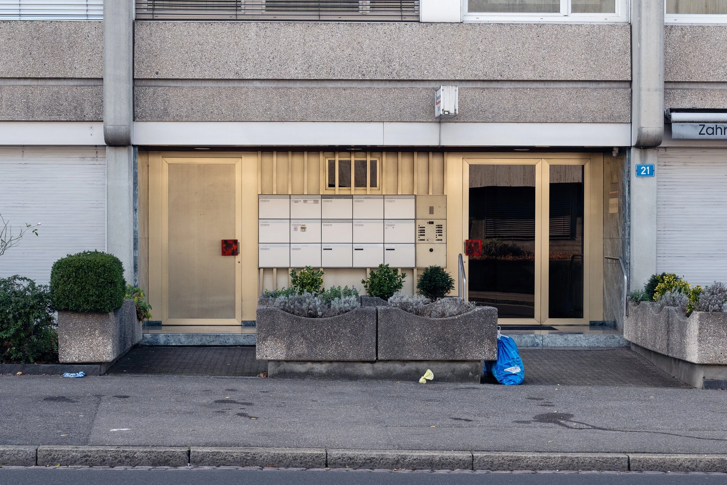 An entrance to a residential building in Basel with mail boxes and a trash bag in front of it