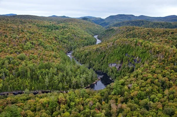 Aerial view of the Hudson River in the Adirondacks showing winding rapids and forested mountains, popular for whitewater rafting trips in New York.
