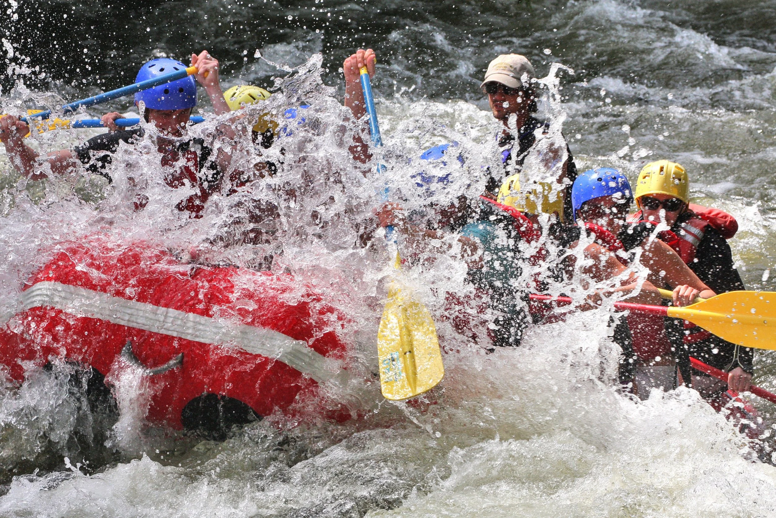 Group of people whitewater rafting on the Hudson River, wearing helmets and life jackets, with splashing water around.