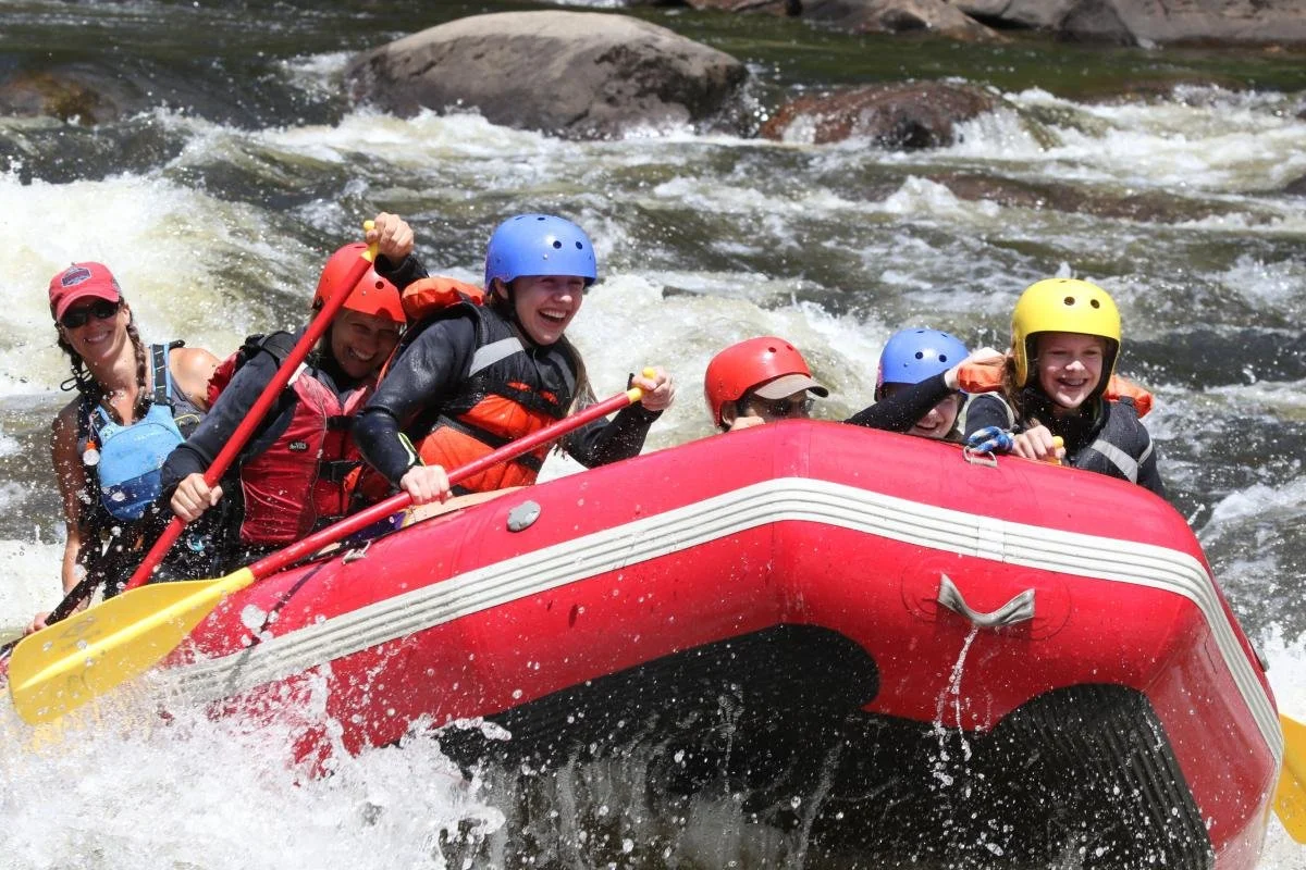 Group of six people wearing helmets and life jackets white water rafting on the Hudson River.