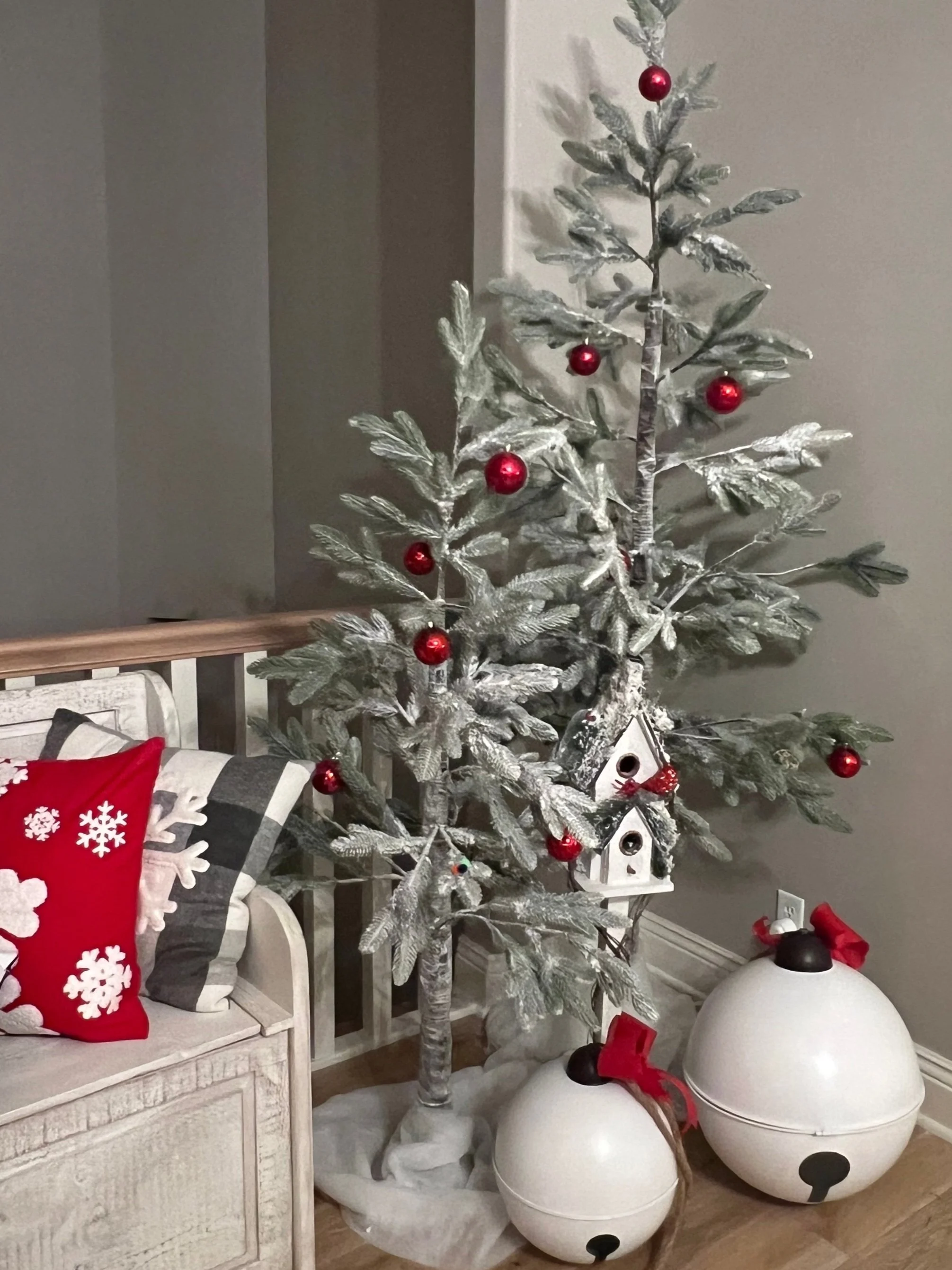 Decorated artificial Christmas tree with red ornaments, white birdhouse decorations, and holiday pillows on a nearby bench.