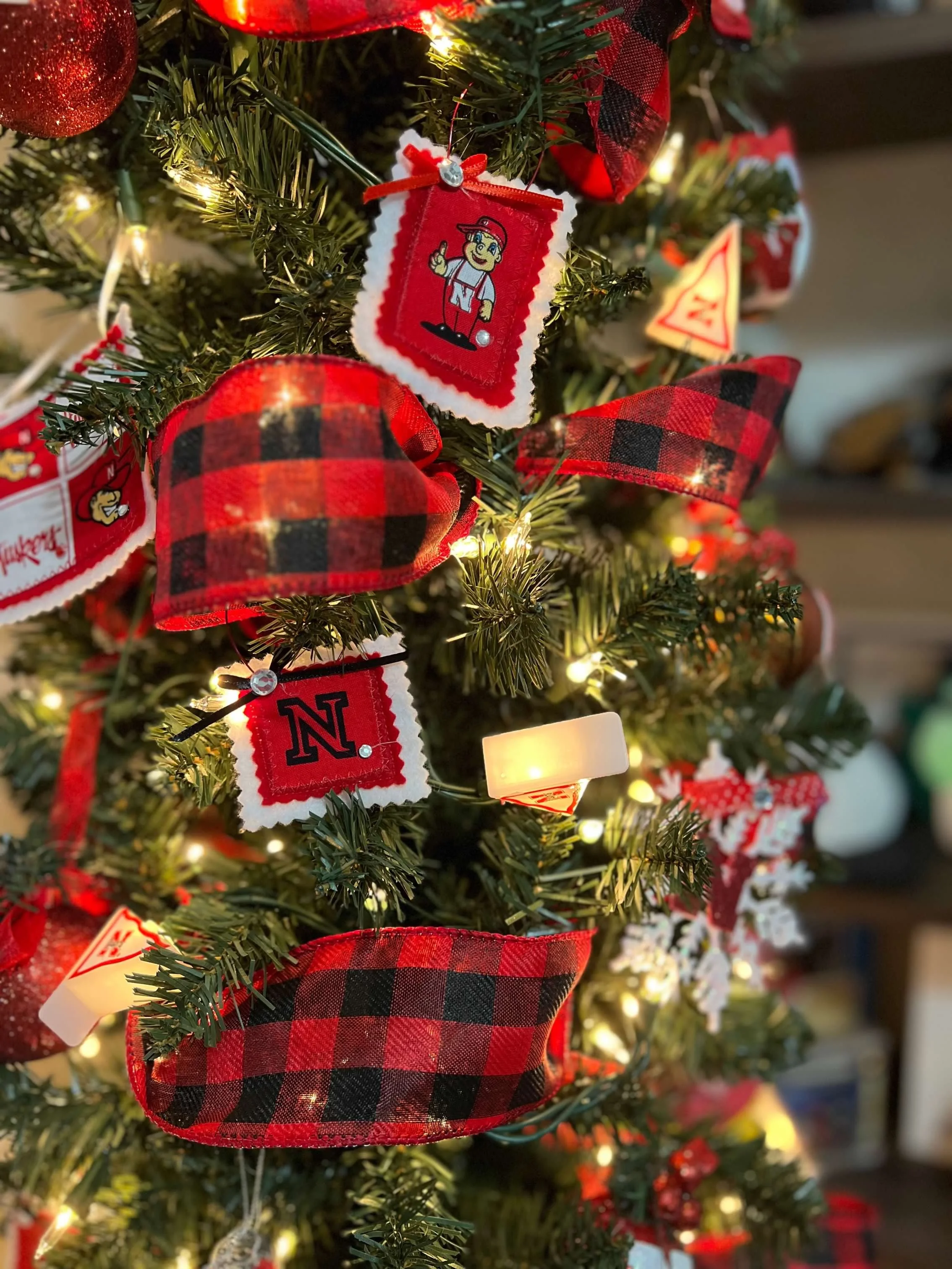 Close-up of a decorated Christmas tree with red and black buffalo plaid ribbons, plush ornaments, and warm string lights.