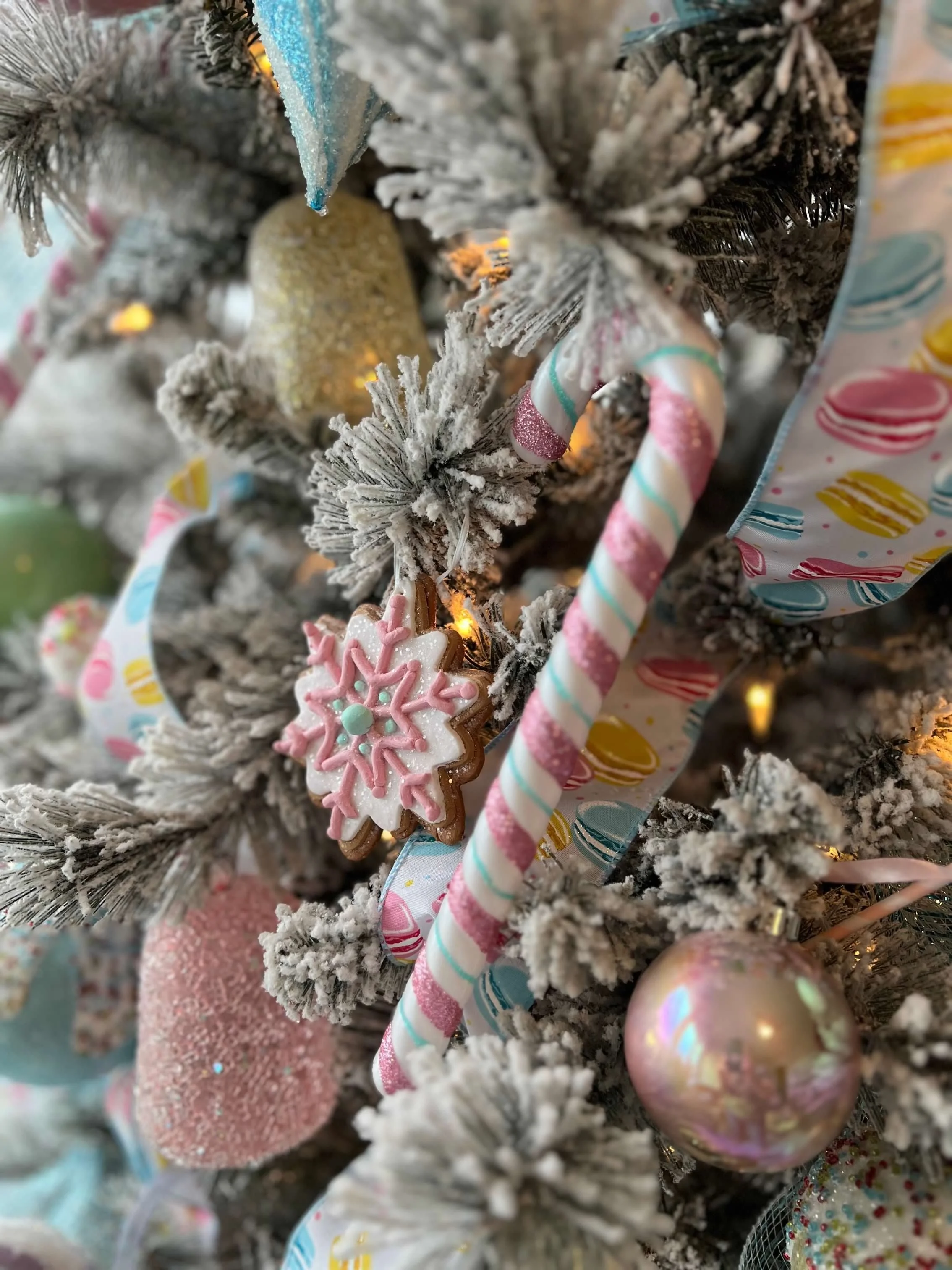 Decorated Christmas tree with pink, white, and gold ornaments, candy cane decorations, snowflake cookies, and a colorful ribbon.