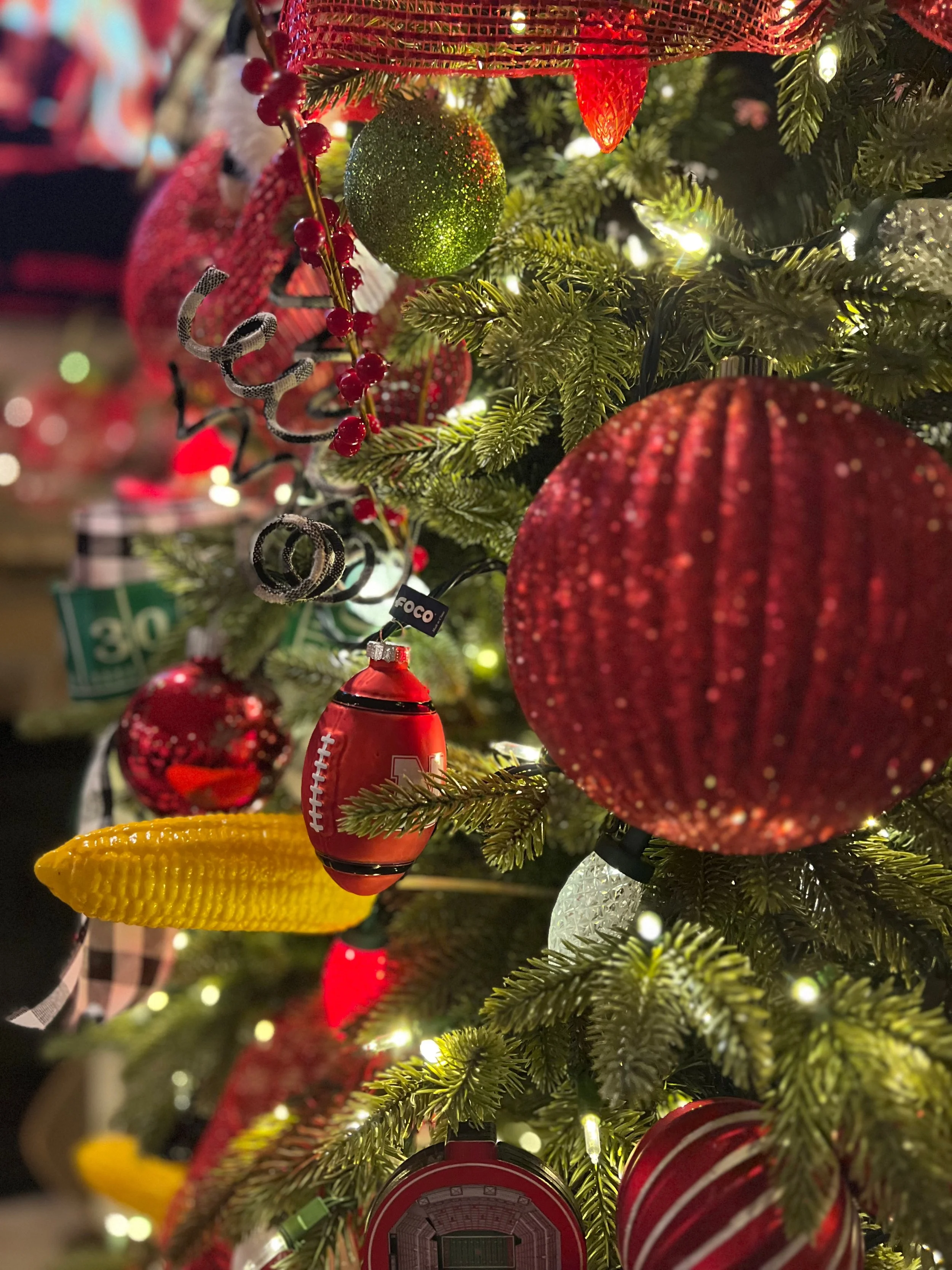 Close-up of decorated Christmas tree with red, green, yellow, and white ornaments, lights, and various holiday-themed decorations.