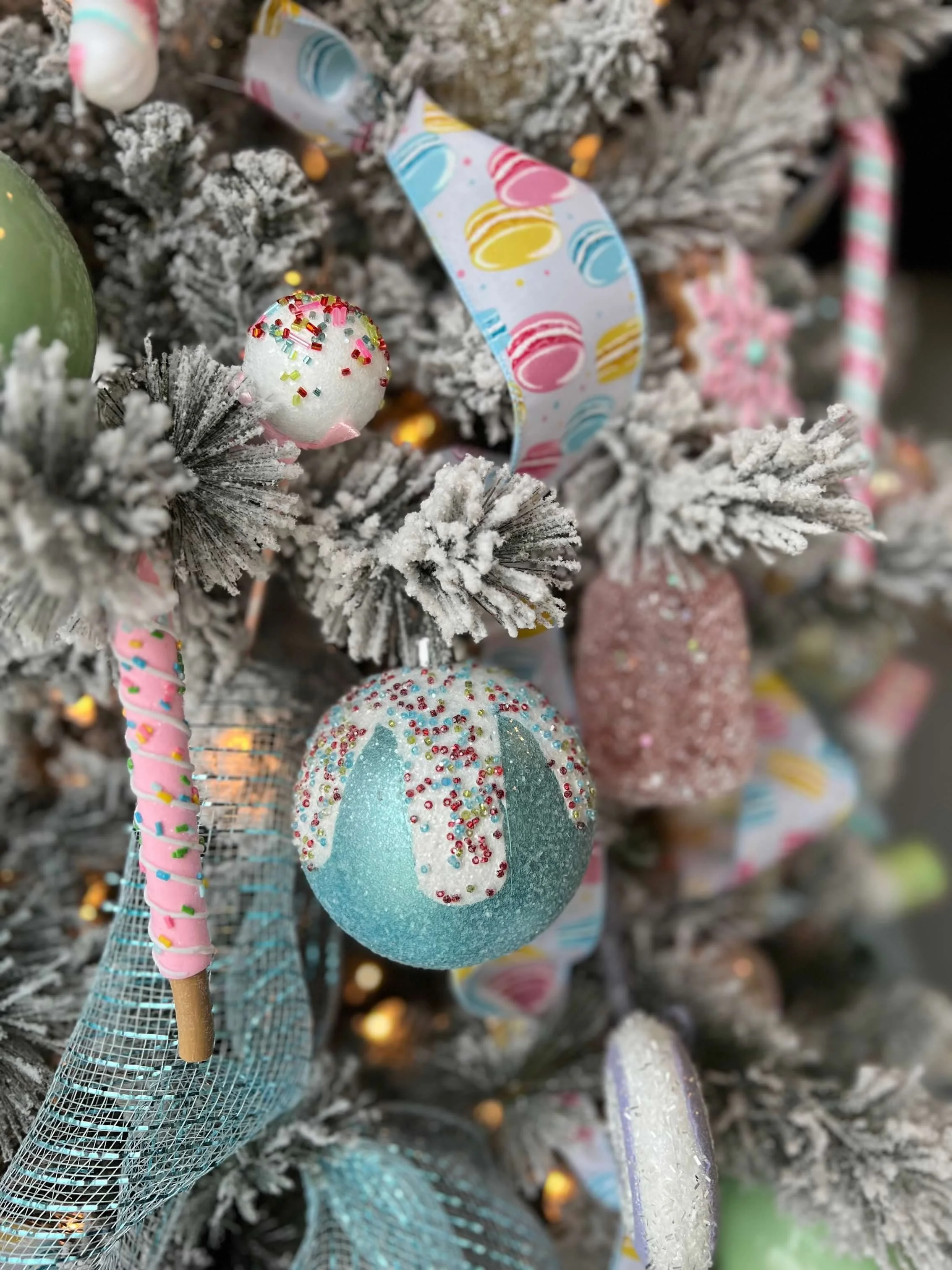 Decorated Christmas tree with frosted branches, colorful ornaments, and ribbons, including a blue spherical ornament with pink and red sprinkles.