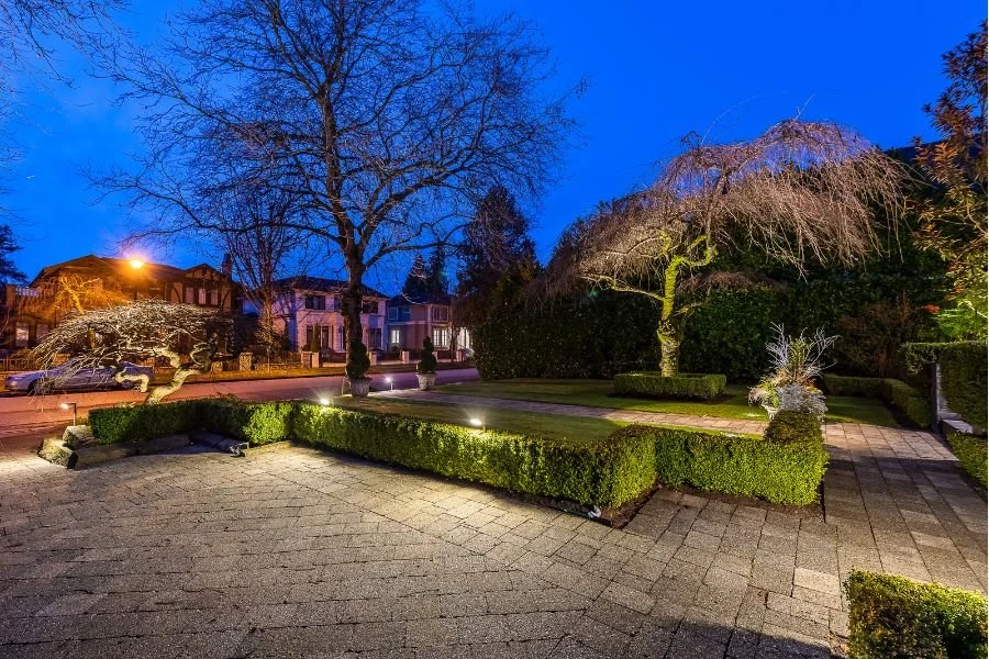 Beautifully lit residential front yard at dusk featuring pathway and hedge lighting, sculpted boxwood landscaping, and accent lighting on bare ornamental trees in a high-end Vancouver neighbourhood.