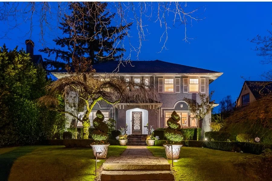Elegant two-storey home in Vancouver beautifully illuminated at dusk with architectural lighting, highlighting the pathway, sculpted trees, entryway, and façade to enhance curb appeal and evening ambience.