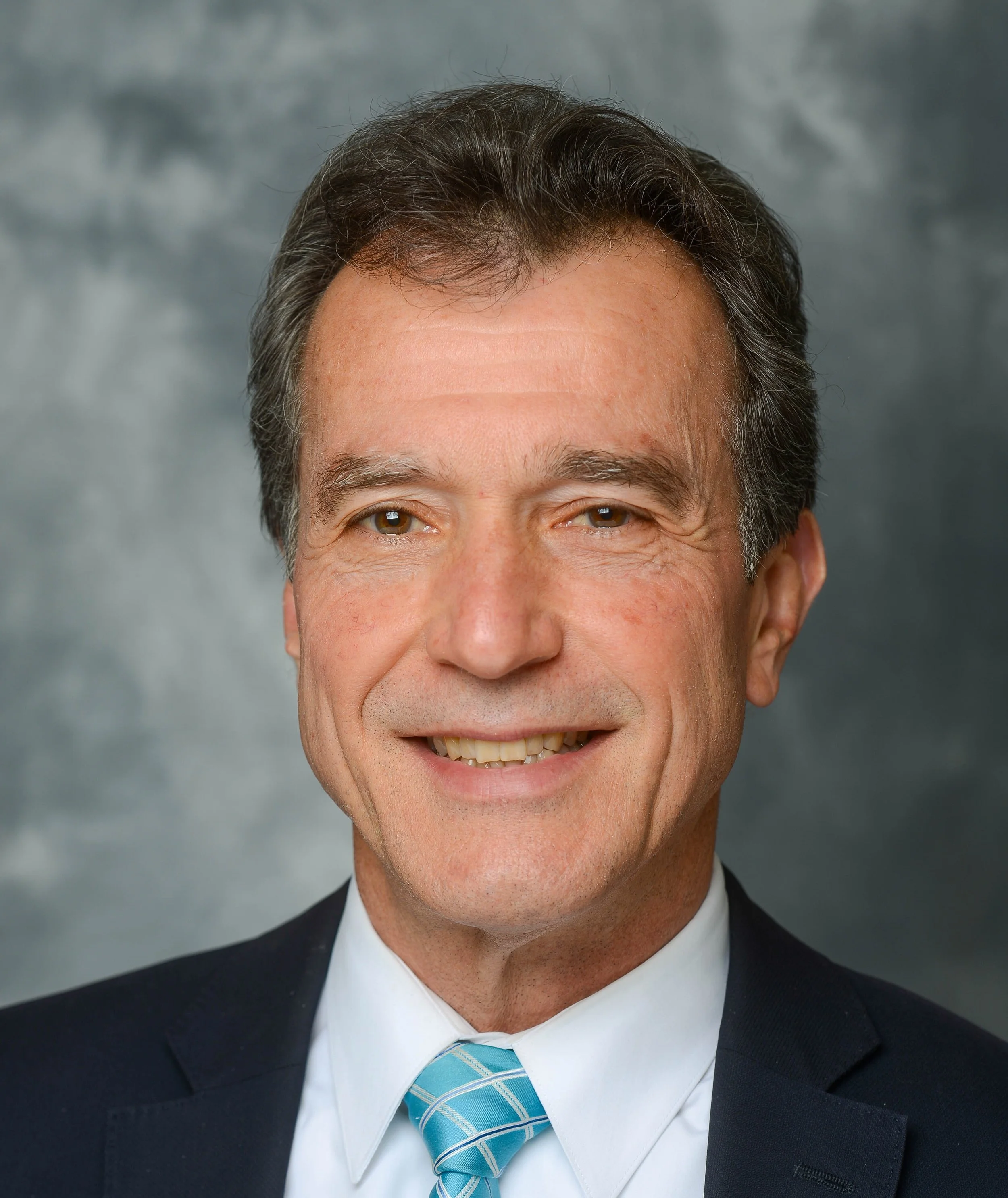 A middle-aged man in a suit and light blue tie smiling at the camera.