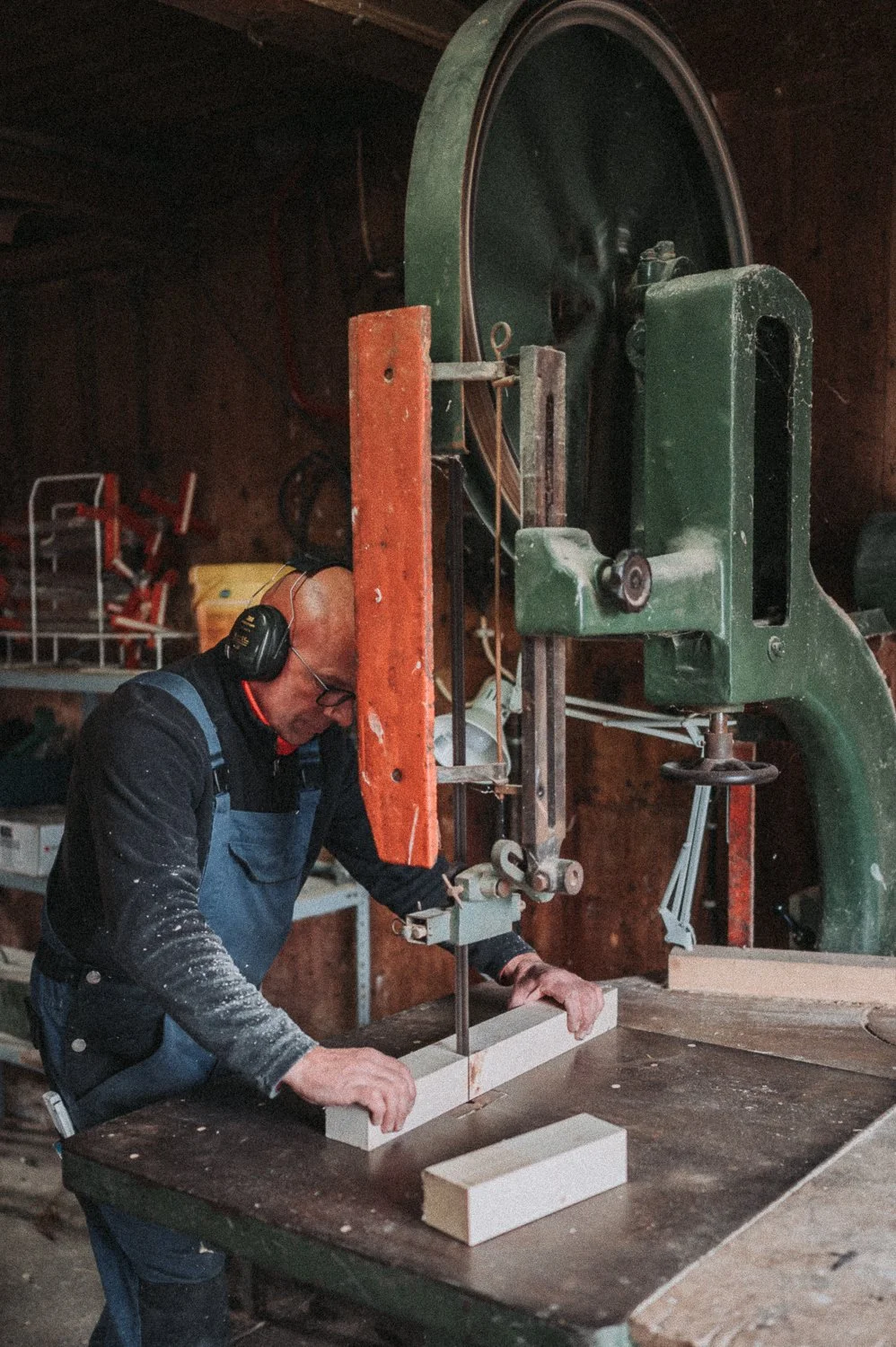 Ein Mann arbeitet in einer Holzwerkstatt mit einer Bandsäge. Er trägt Gehörschutz und arbeitet an einem Stück Holz.