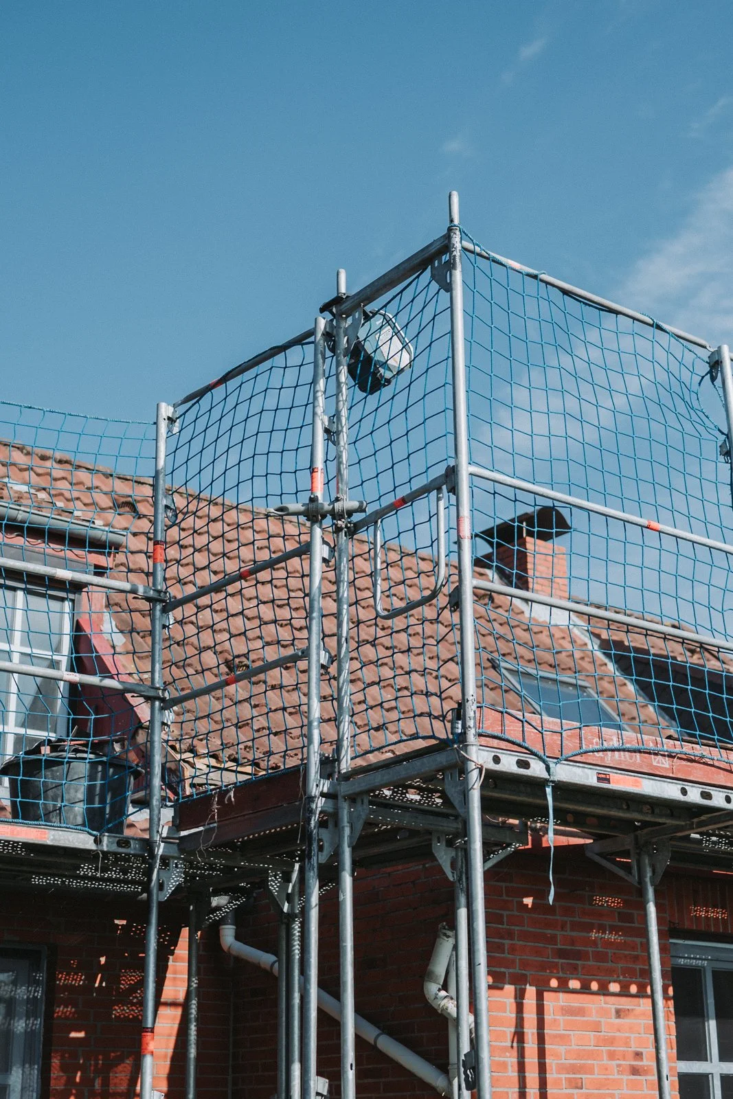 Gerüst vor einem roten Backsteinhaus mit Dachfenstern, blauer Himmel im Hintergrund.