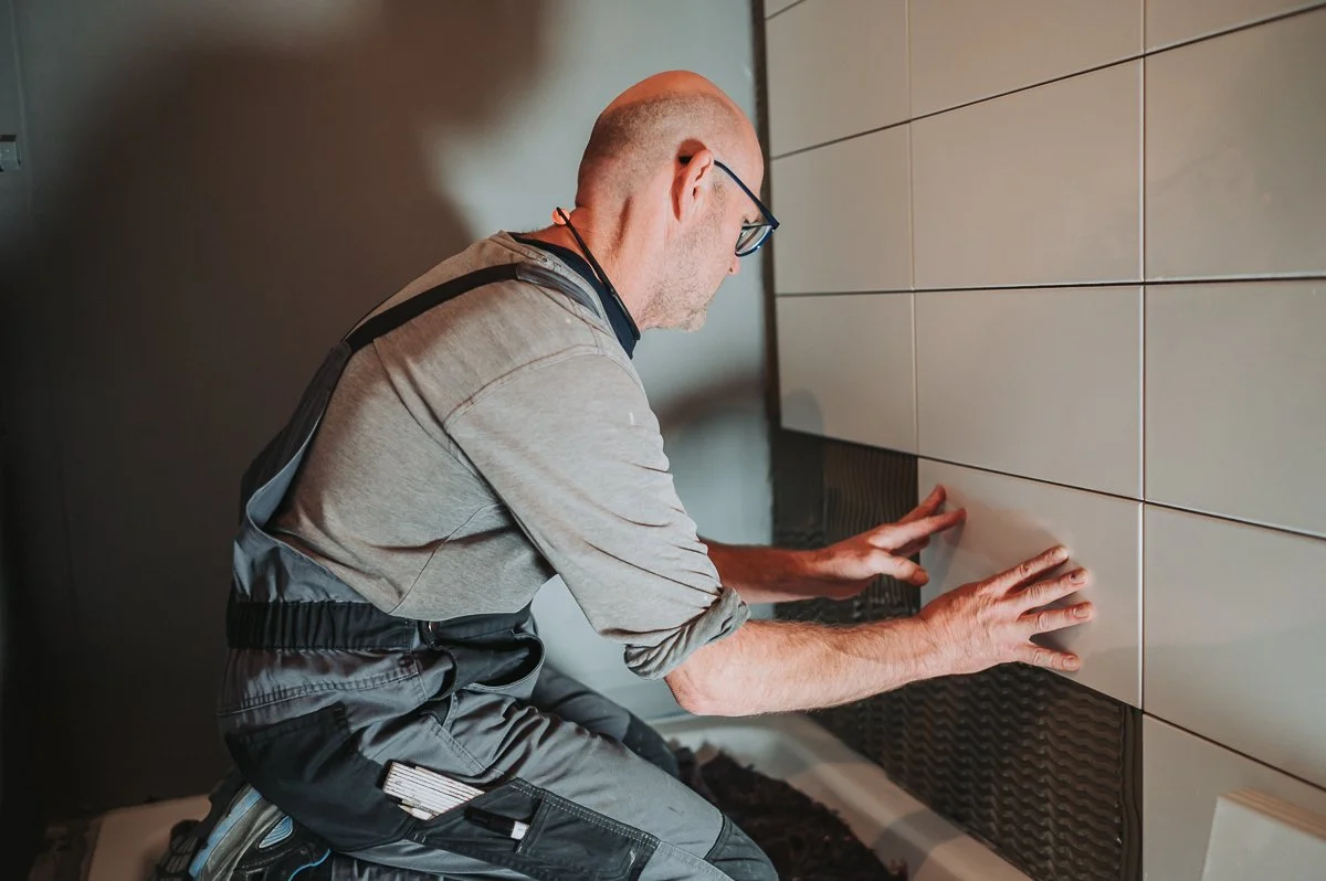 Mann legt Fliese an eine Wand in einem Raum.