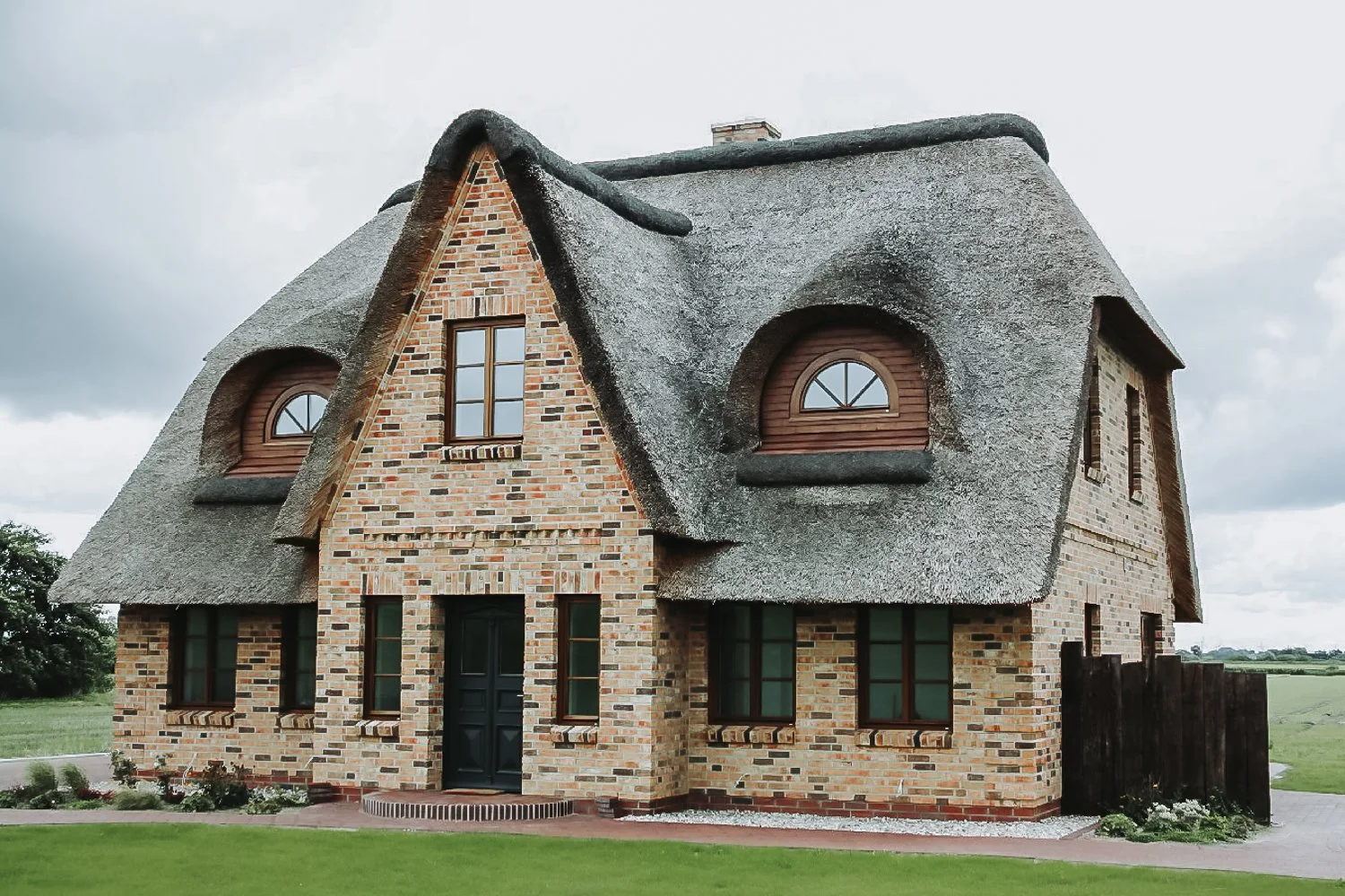 Ein Haus mit Ziegelfassade und Satteldach, das mit Strohdach bedeckt ist, in einer ländlichen Umgebung.