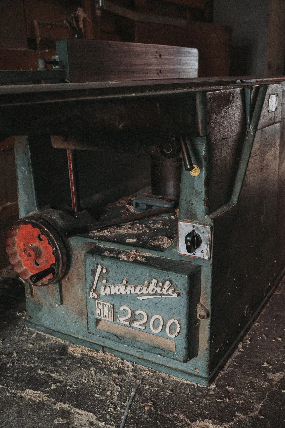 Alte, verstaubte Tischkreissäge mit abgenutztem Gehäuse, Markenname 'Lurzindale' und Modell 'SCM 2200', in einem dunklen, staubigen Raum.