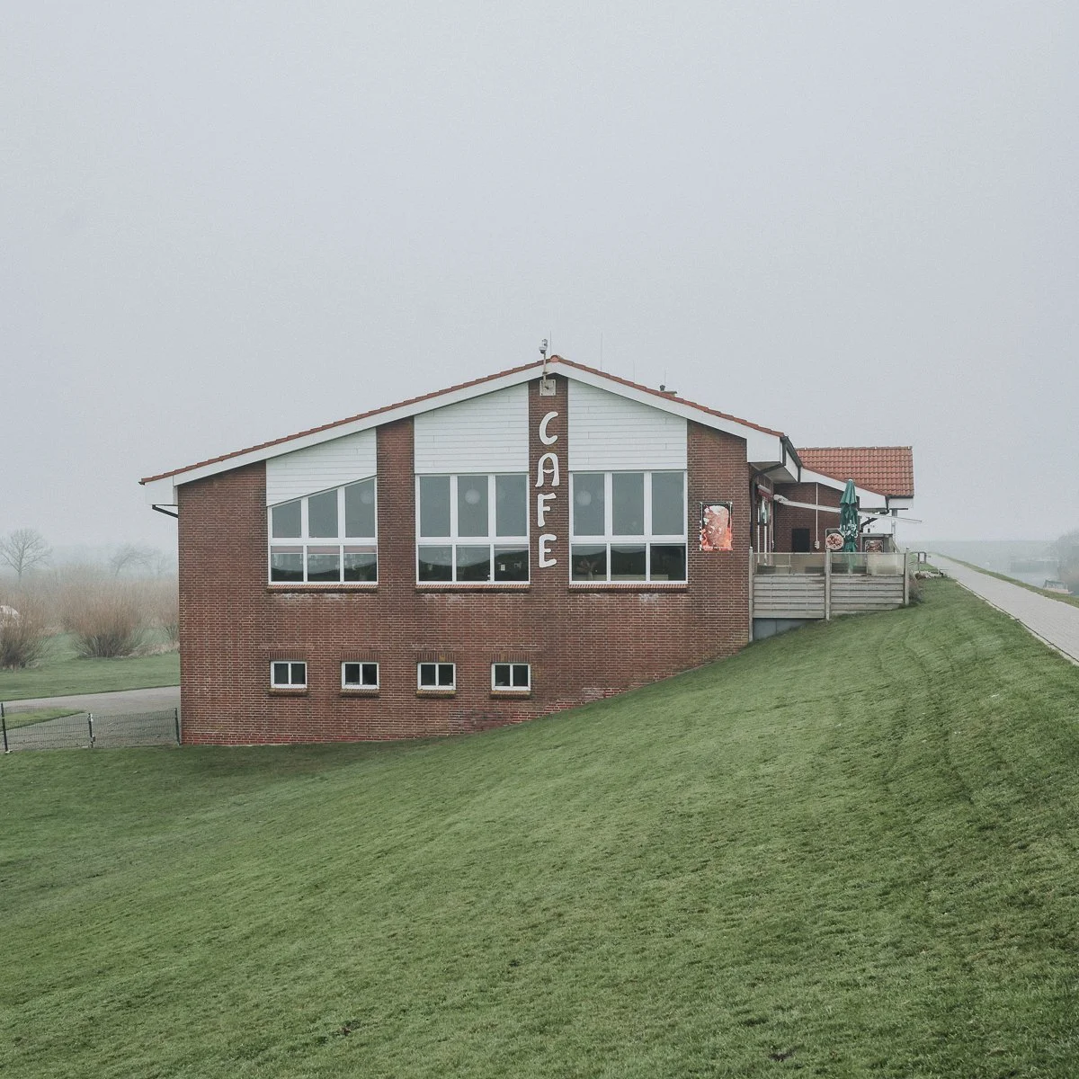 Ein Restaurantgebäude mit einem großen vertikalen Schild, auf dem 'CAFE' steht, an einem bewölkten Tag auf einer grünen Hügellandschaft.