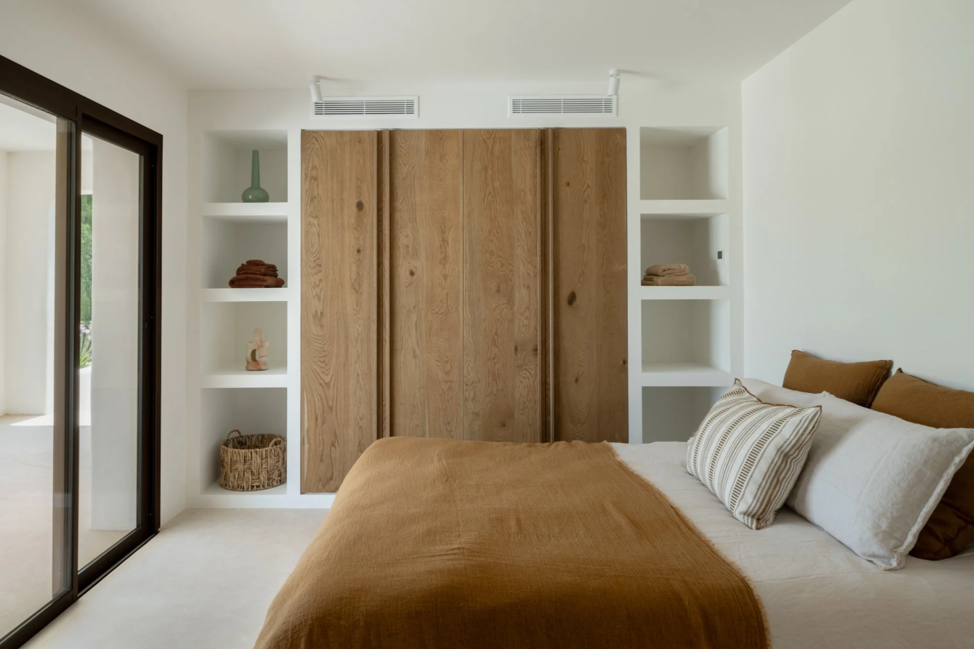 A bedroom with a warm designed interior and decoration. wooden closet doors and shelves that are decorated with curated decorations. 