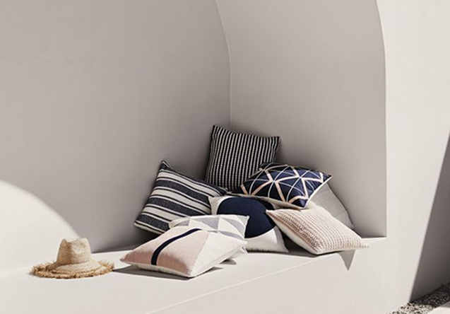 A white built-in bench with several decorative pillows and a straw sun hat on it.